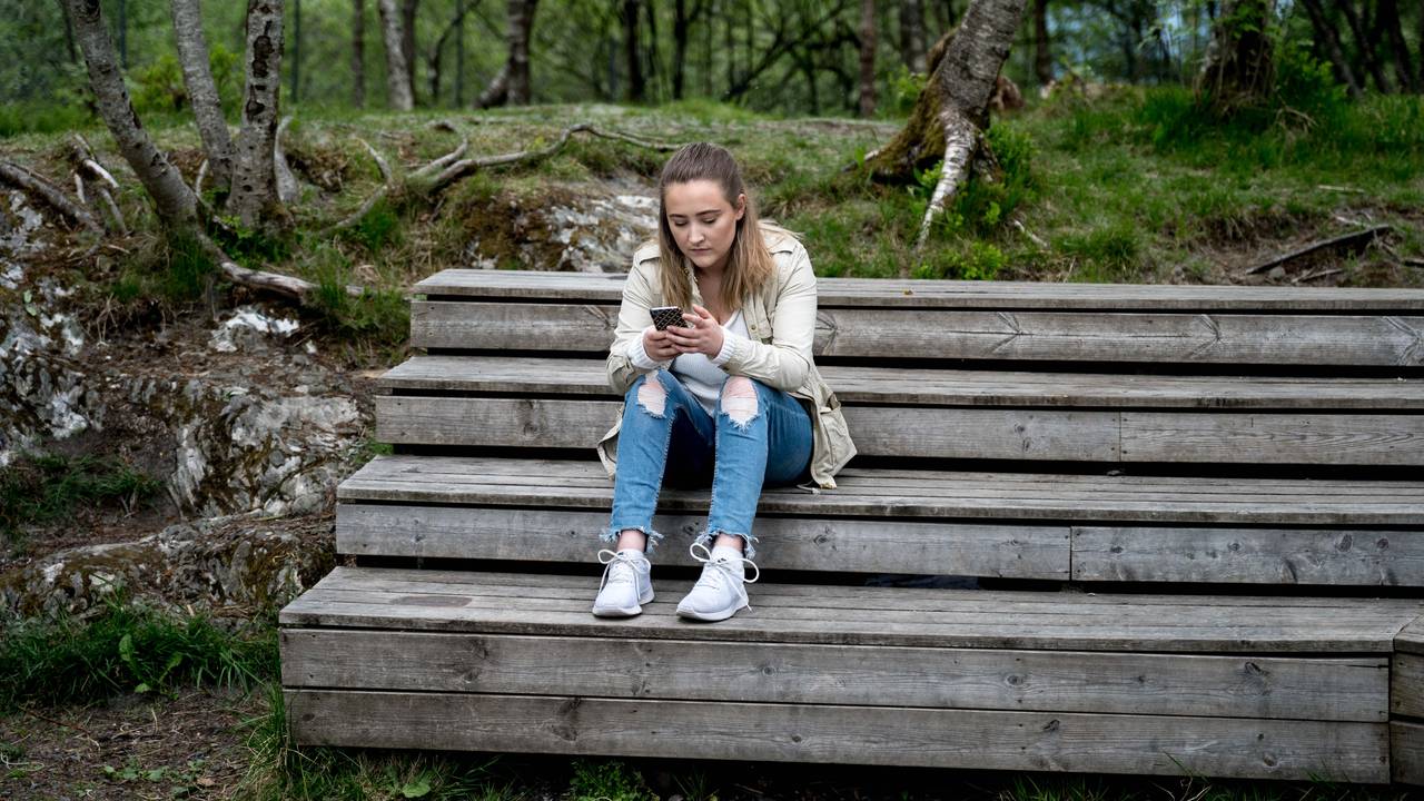 Bilde av Ingebjørg som sitter på en trappeaktig benk i skogen