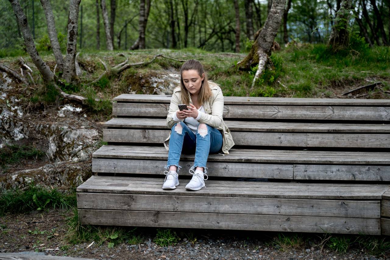Bilde av Ingebjørg som sitter på en trappeaktig benk i skogen