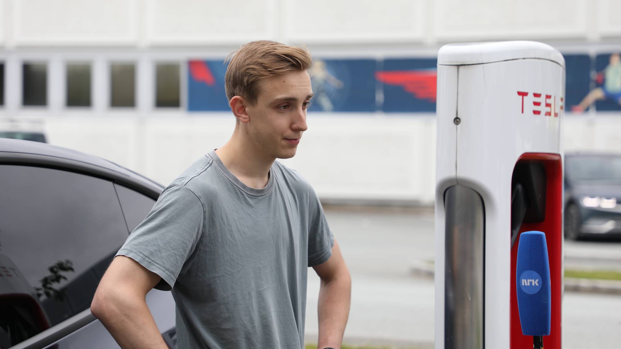 Daniel Hansen står foran en Tesla og en Tesla-lader.