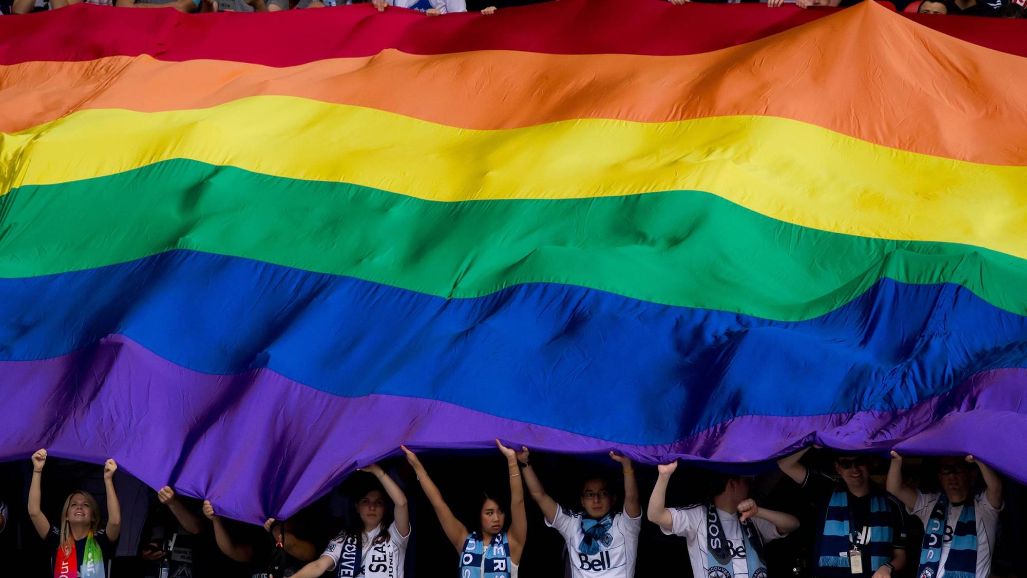 Fans support an oversized rainbow flag before the Vancouver Whitecaps play the Seattle Sounders in an MLS soccer game in Vancouver.
