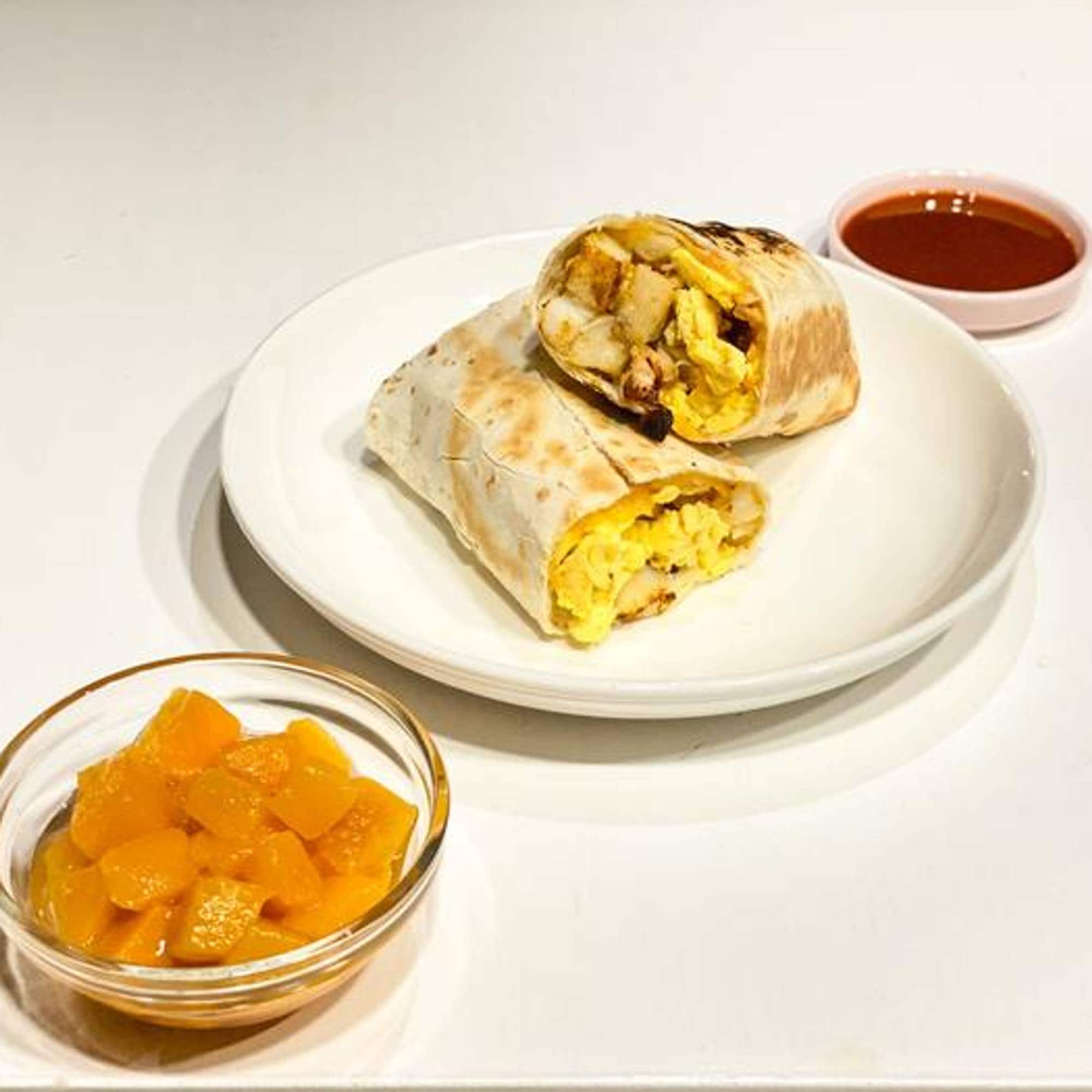 Bildet viser et måltid bestående av en burrito med egg og frukt i en skål.