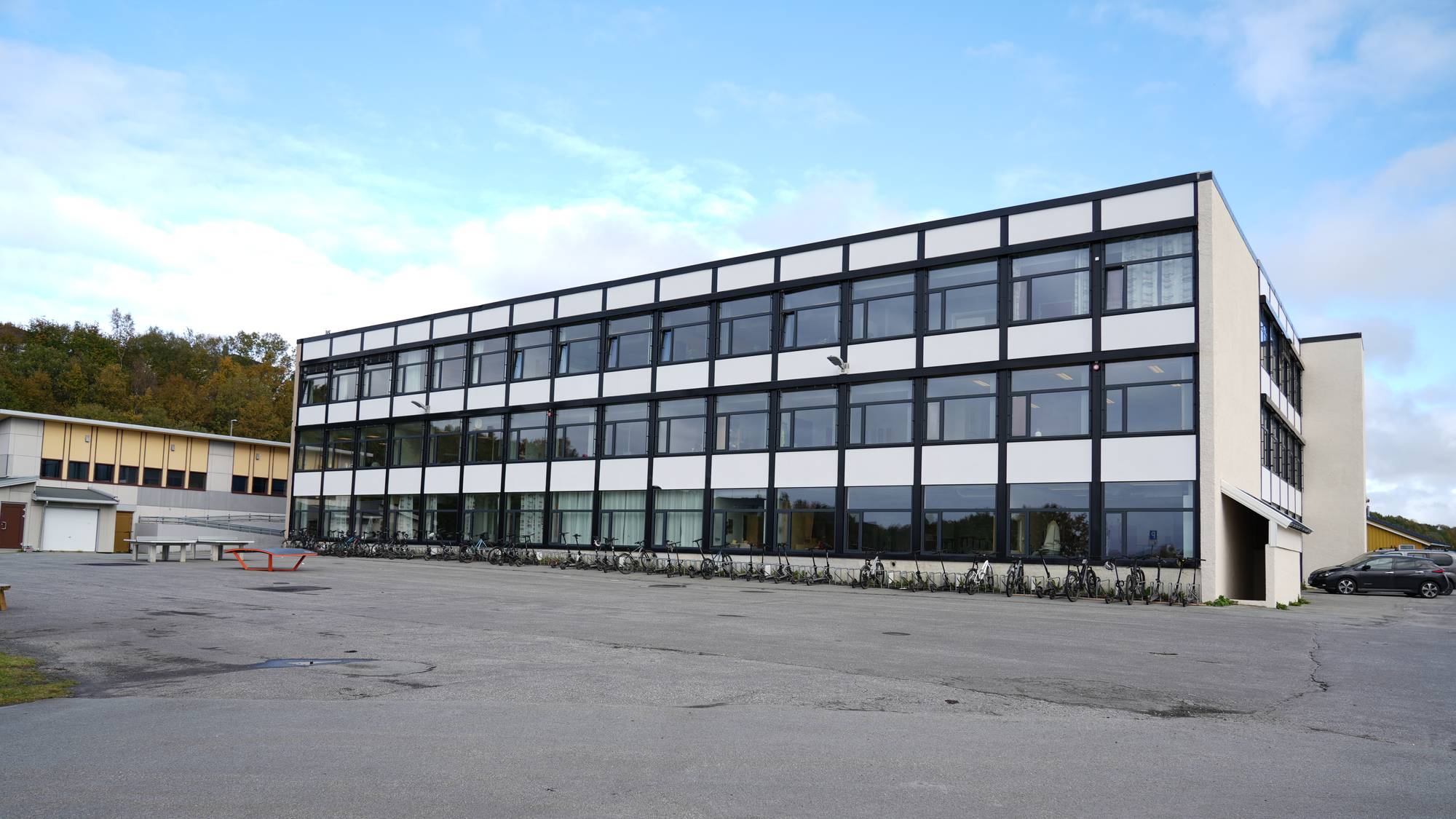 Skolebygg med tre etasjer og mange vinduer, med en rad av sykler parkert foran bygget. (Bildebeskrivelsen er laget av en KI-tjeneste)