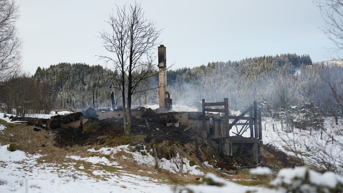 Et brennende hus står igjen som en ruin, med røykskyer som stiger opp fra det nedbrente området. Området er dekket av snø, med trær og fjell i bakgrunnen. Ingen personer er synlige i bildet. Skadene er omfattende, og bare deler av bygningens struktur er intakt. (Bildebeskrivelsen er laget av en KI-tjeneste) FOTO: Nina Kausland/NRK