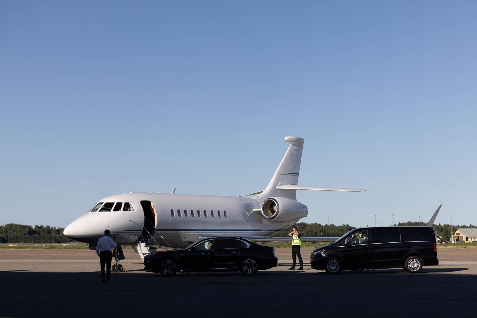 Et hvitt privatfly på med døren åpen. Foran står sto mørke biler og en mann i refleksivest. 