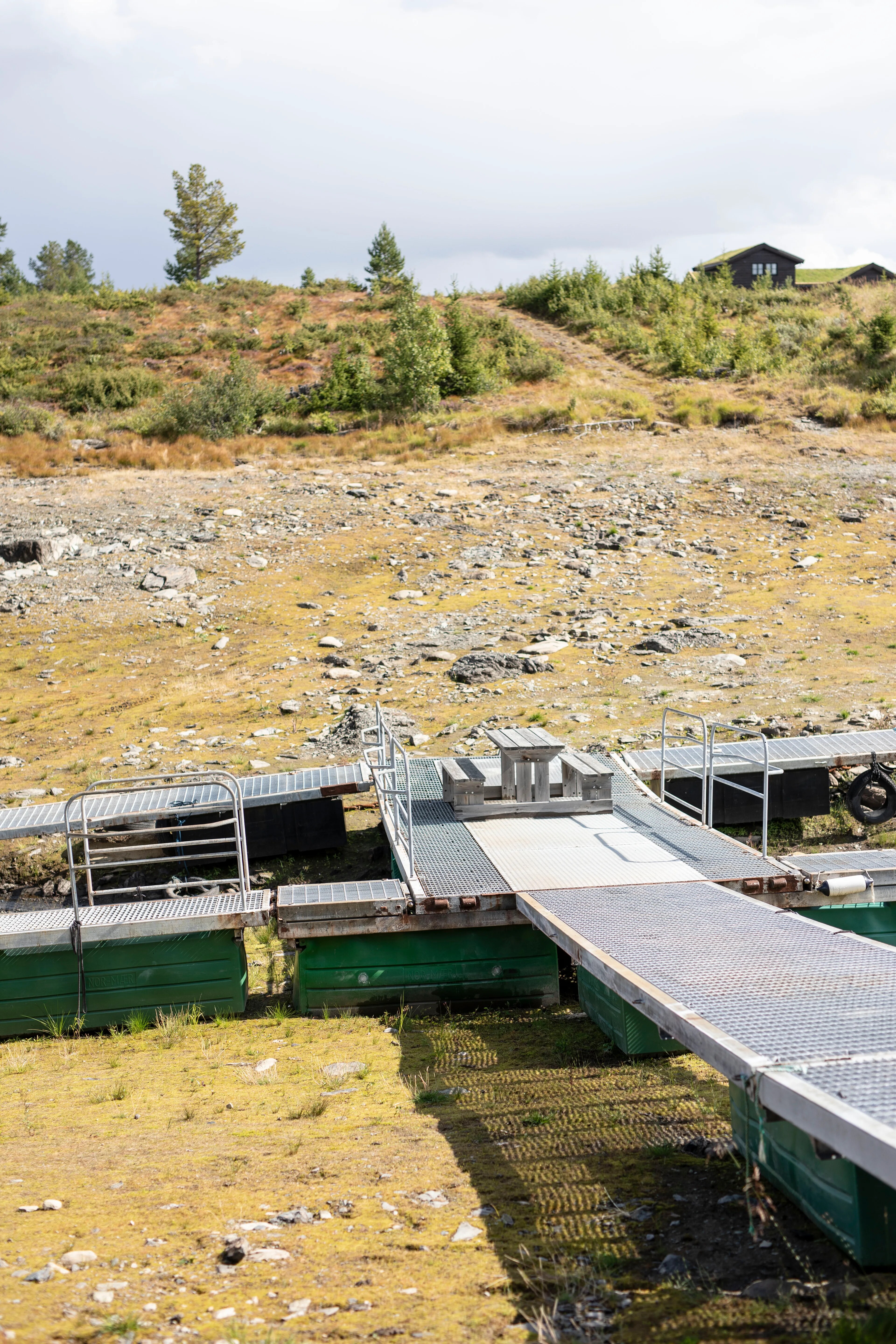 En flytebrygge ligger på land der det vanligvis er vann ved normal vannstand. På brygga står et  piknikbord.