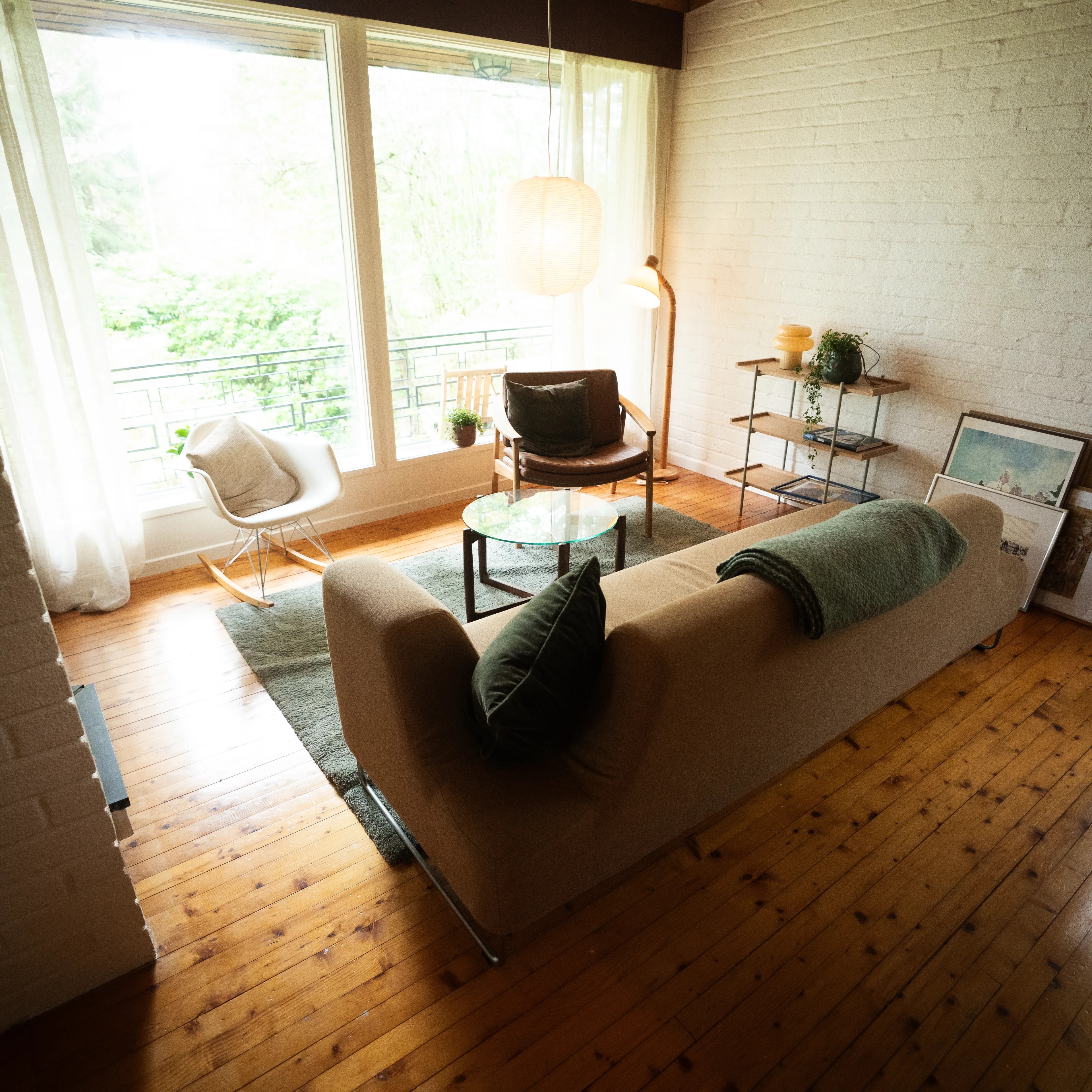 Stue med sofa, lenestoler og et lite bord foran store vinduer med utsikt til uteområde. (Bildebeskrivelsen er laget av en KI-tjeneste)