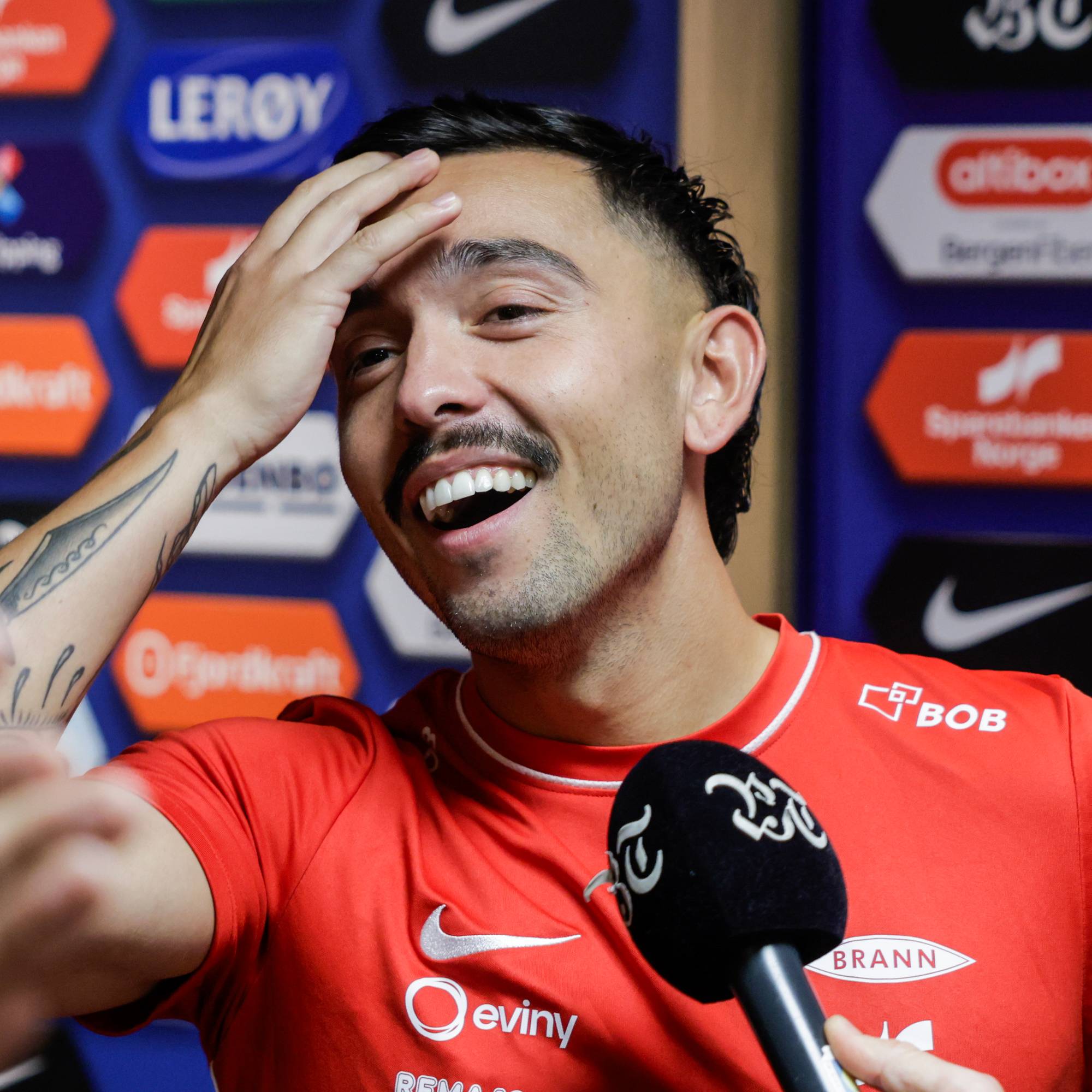 Brann-spiller Niklas Castro smiler og tar seg til pannen under et intervju. 
