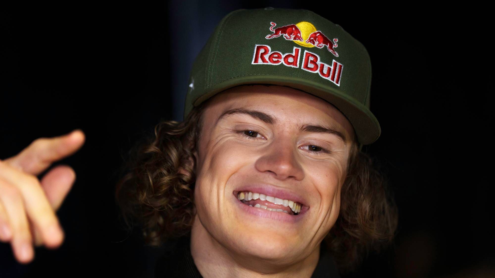 En smilende mann med krøllete hår iført en grønn Red Bull-caps. Han peker mot kameraet. (Bildebeskrivelsen er laget av en KI-tjeneste)