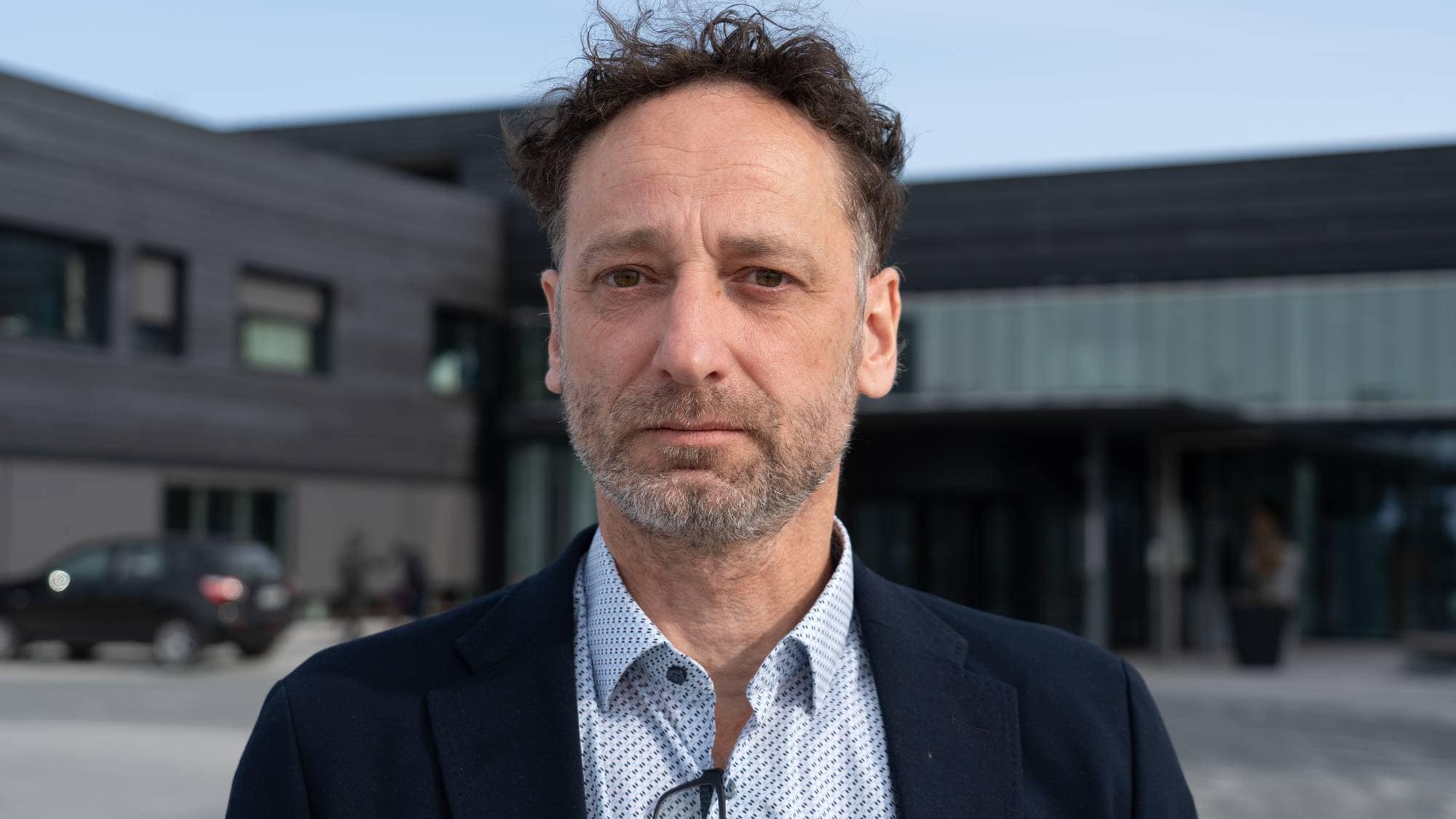 en mann i dress står foran en stor svart bygning. 