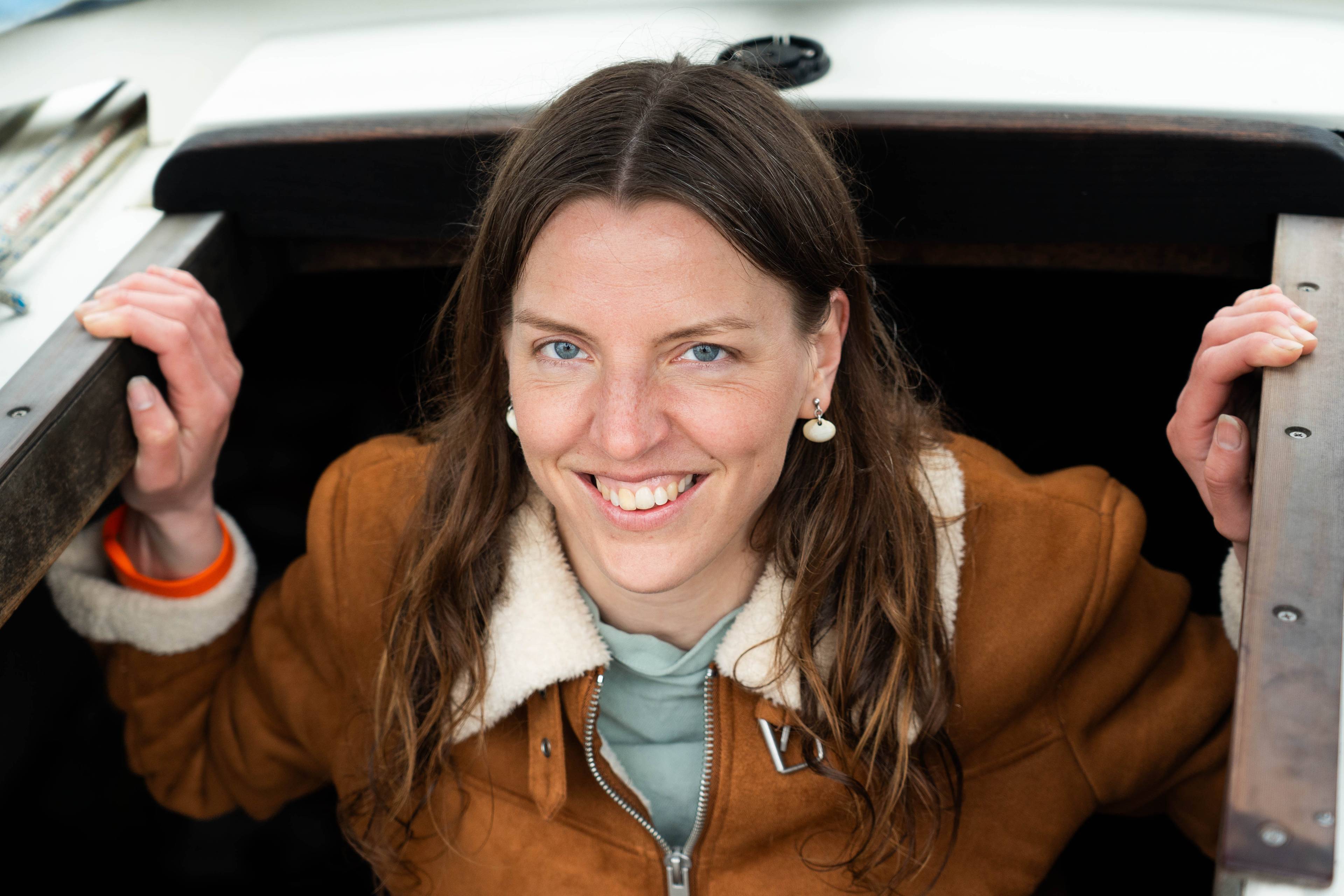 En dame med brunt hår beveger seg opp fra underetasjen i en seilbåt og smiler.
