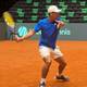 Carl Andreas Wold / NRK Tennisspiller i blå t-skjorte slår et slag på en grusbane i en tom hall. (Bildebeskrivelsen er laget av en KI-tjeneste)