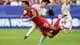 CHARLOTTE WILSON / GETTY IMAGES NORTH AMERICA,NTB Fotballspillere i aksjon. En spiller i rød drakt takles av en spiller i hvit drakt. Bakgrunnen viser en tribune med tilskuere og et FIFA World Cup-banner. (Bildebeskrivelsen er laget av en KI-tjeneste)