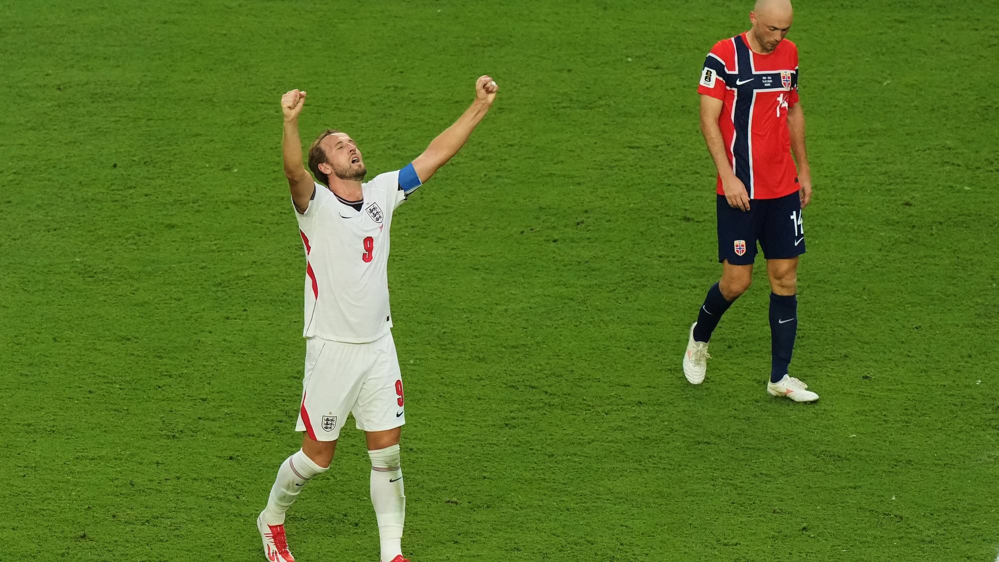 Harry Kane jubler med hevede armer ved siden av en skuffet norsk landslagsspiller på fotballbanen. (Bildebeskrivelsen er laget av en KI-tjeneste)