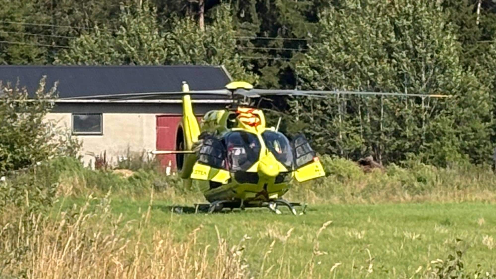 Luftambulanse og ambulanse ved et gårdstun i et skogområde. (Bildebeskrivelsen er laget av en KI-tjeneste)