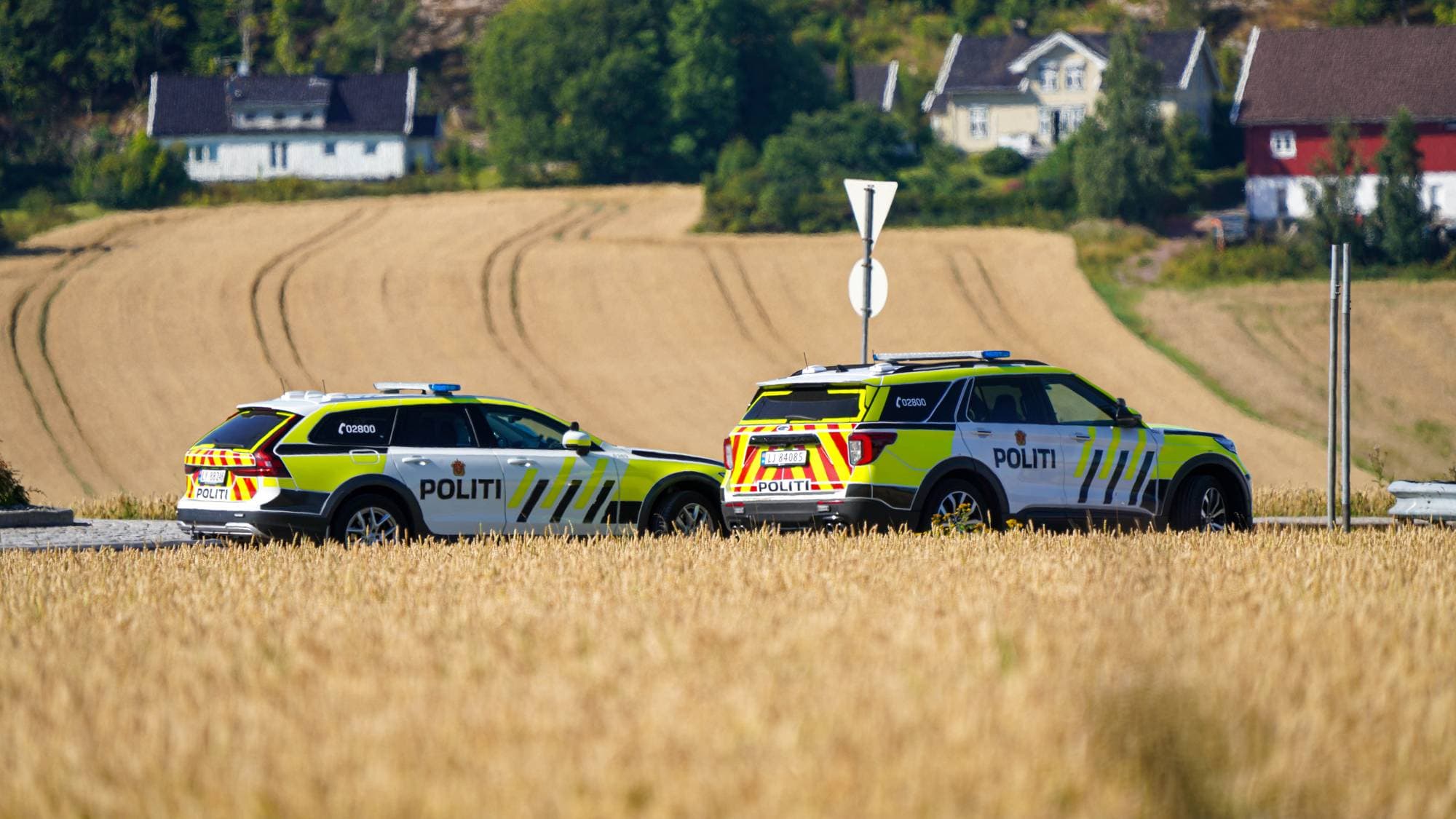 To politibiler står parkert ved en vei. Det er jorder på begge sider av veien.