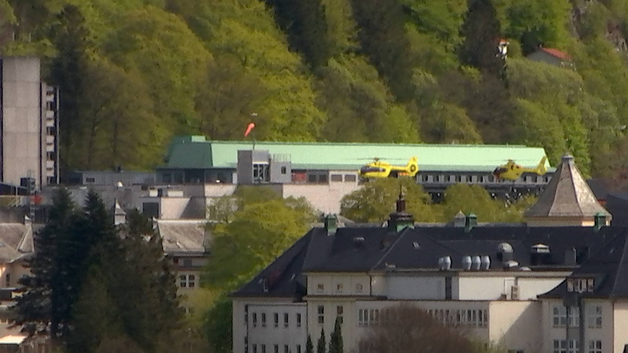 to gule helikopter står på bakken mellom fleire store bygg