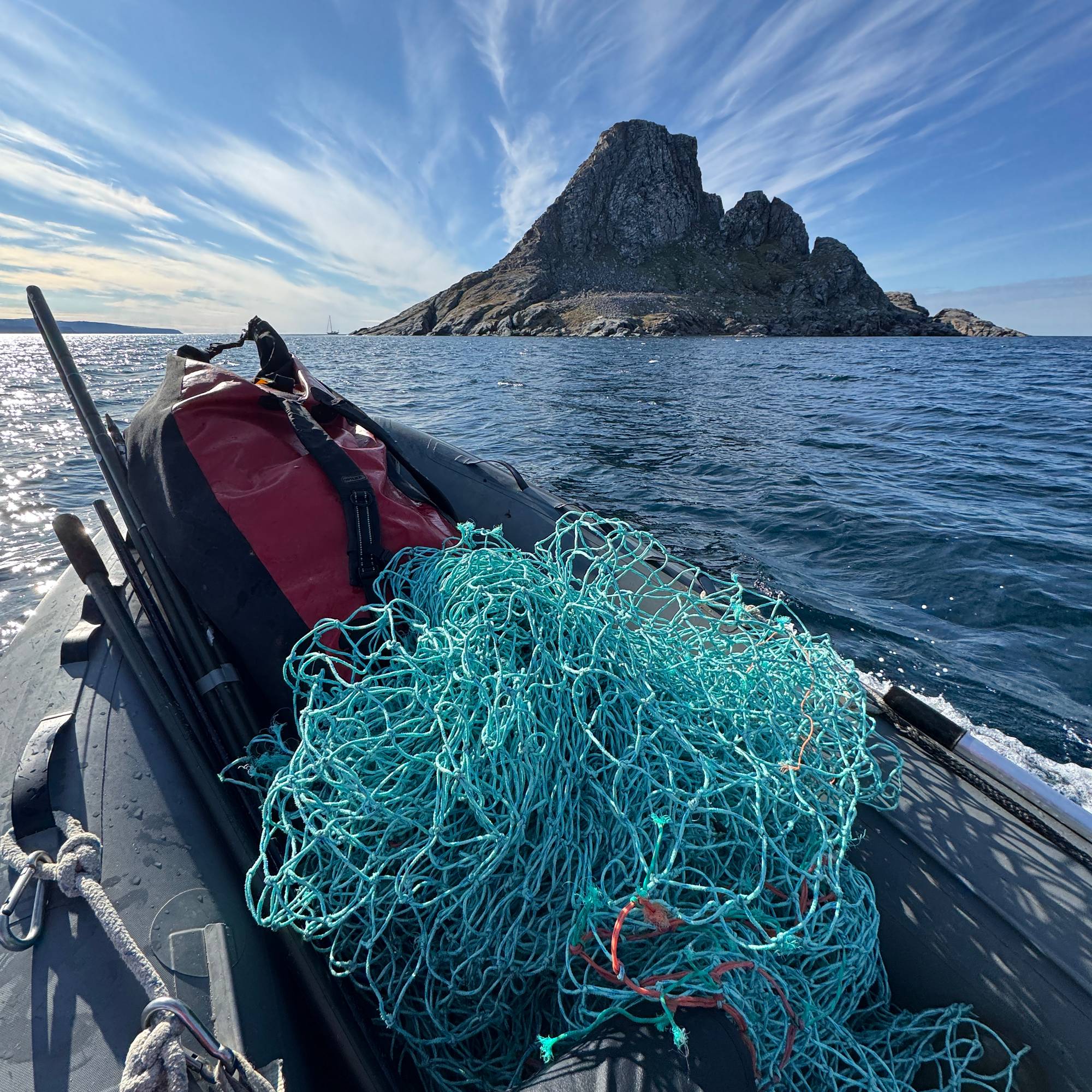 Et fiskegarn ligger i en haug på en rib-båt. Et fjell sees i horisonten av havet.