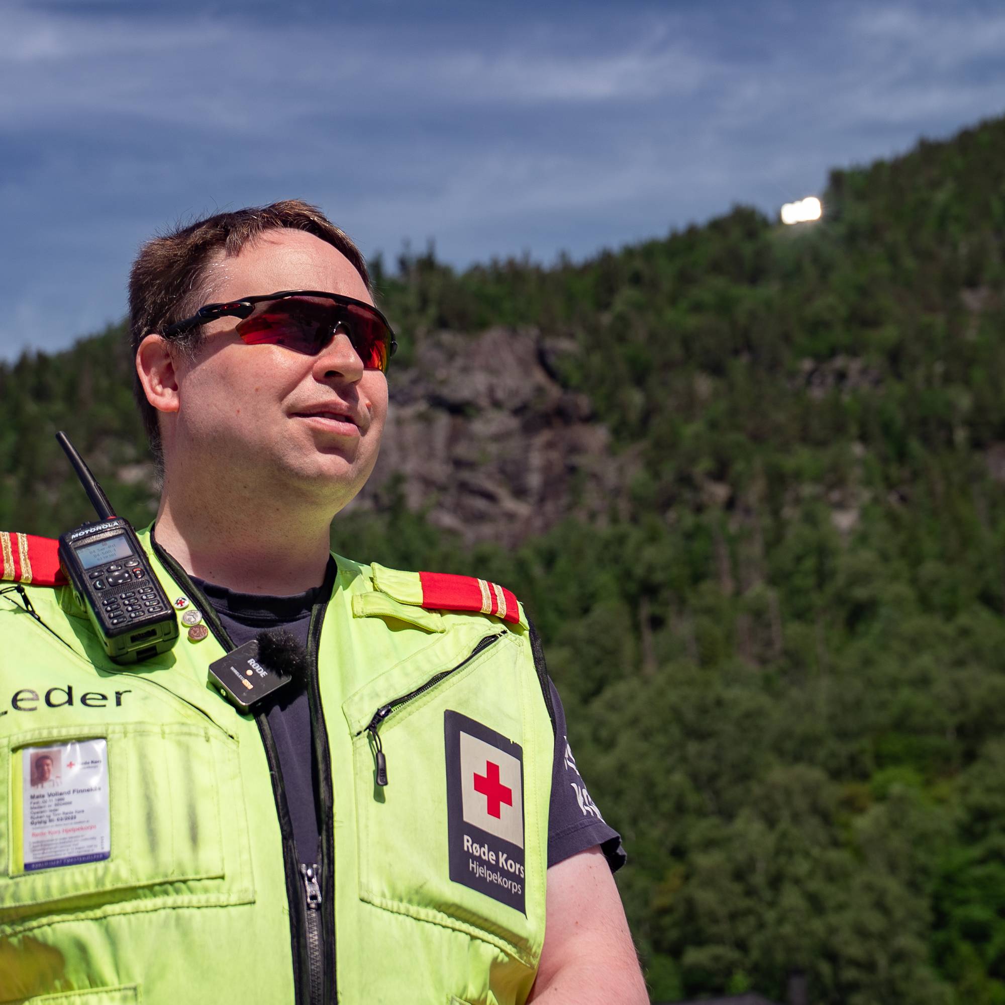 Mann med gul refleksvest har tre speil i en fjellside i Rjukan i bakgrunnen. 