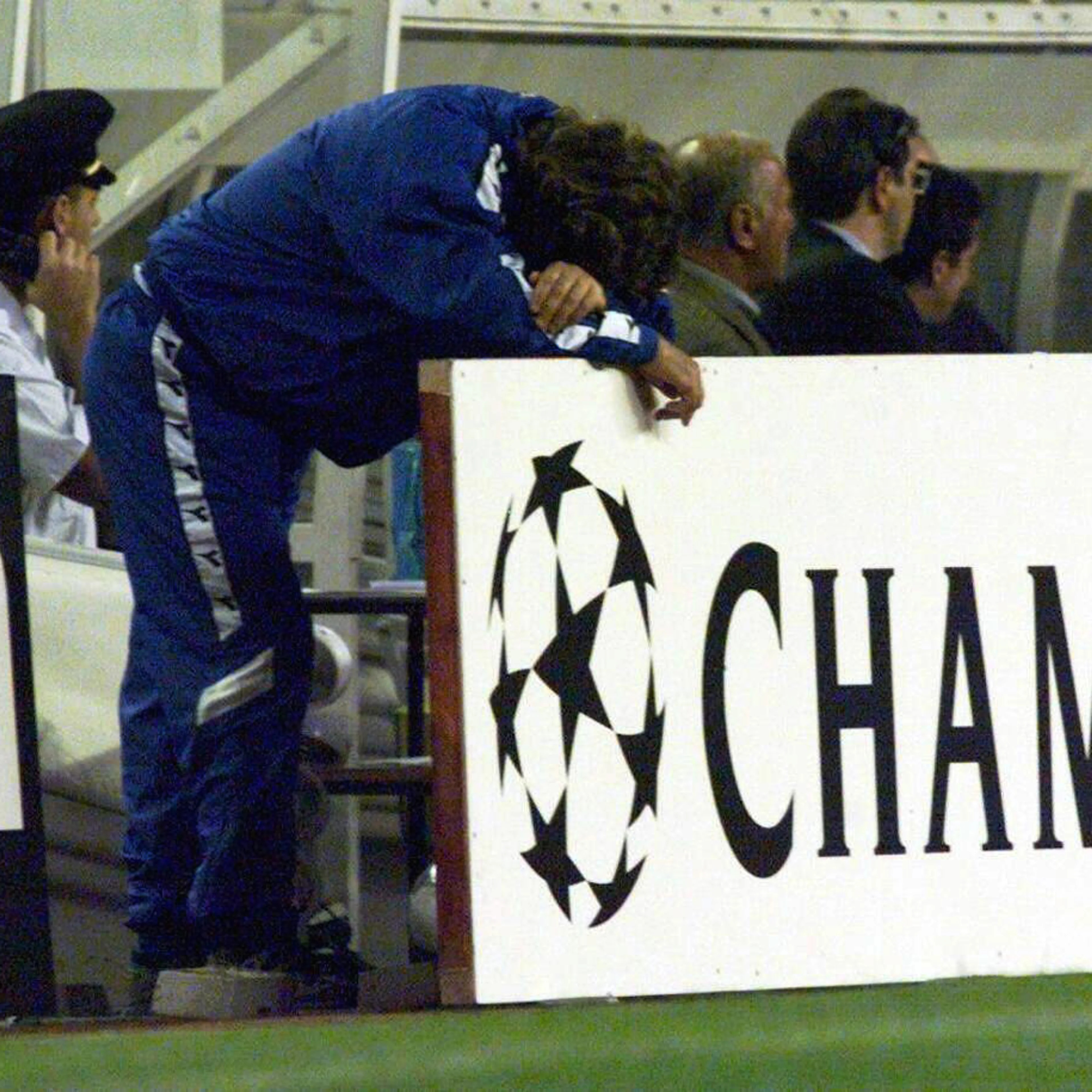 Fotballtrener i blå drakt lener hodet mot en Champions League-reklamevegg på sidelinjen. (Bildebeskrivelsen er laget av en KI-tjeneste)