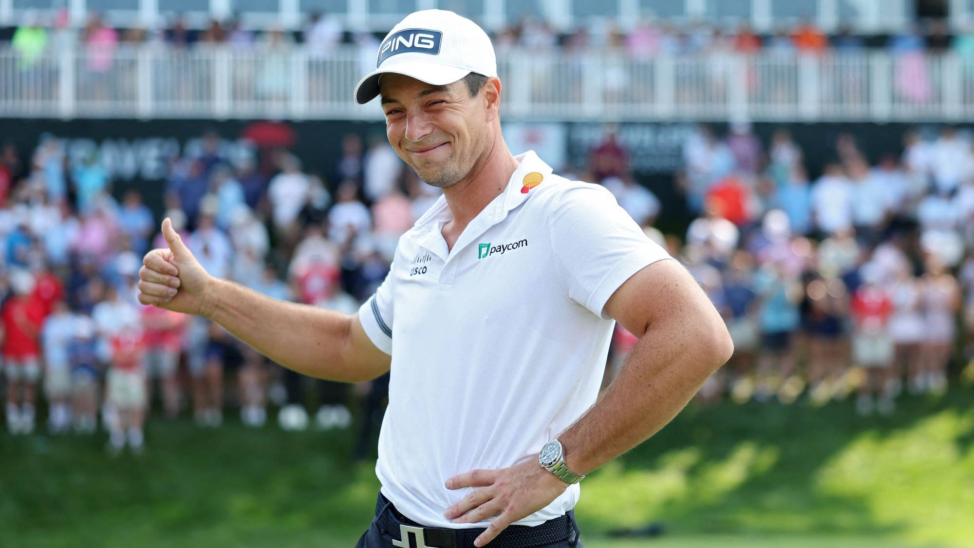 Golfspiller Viktor Hovland smiler og viser tommel opp for publikum på en golfbane. (Bildebeskrivelsen er laget av en KI-tjeneste)