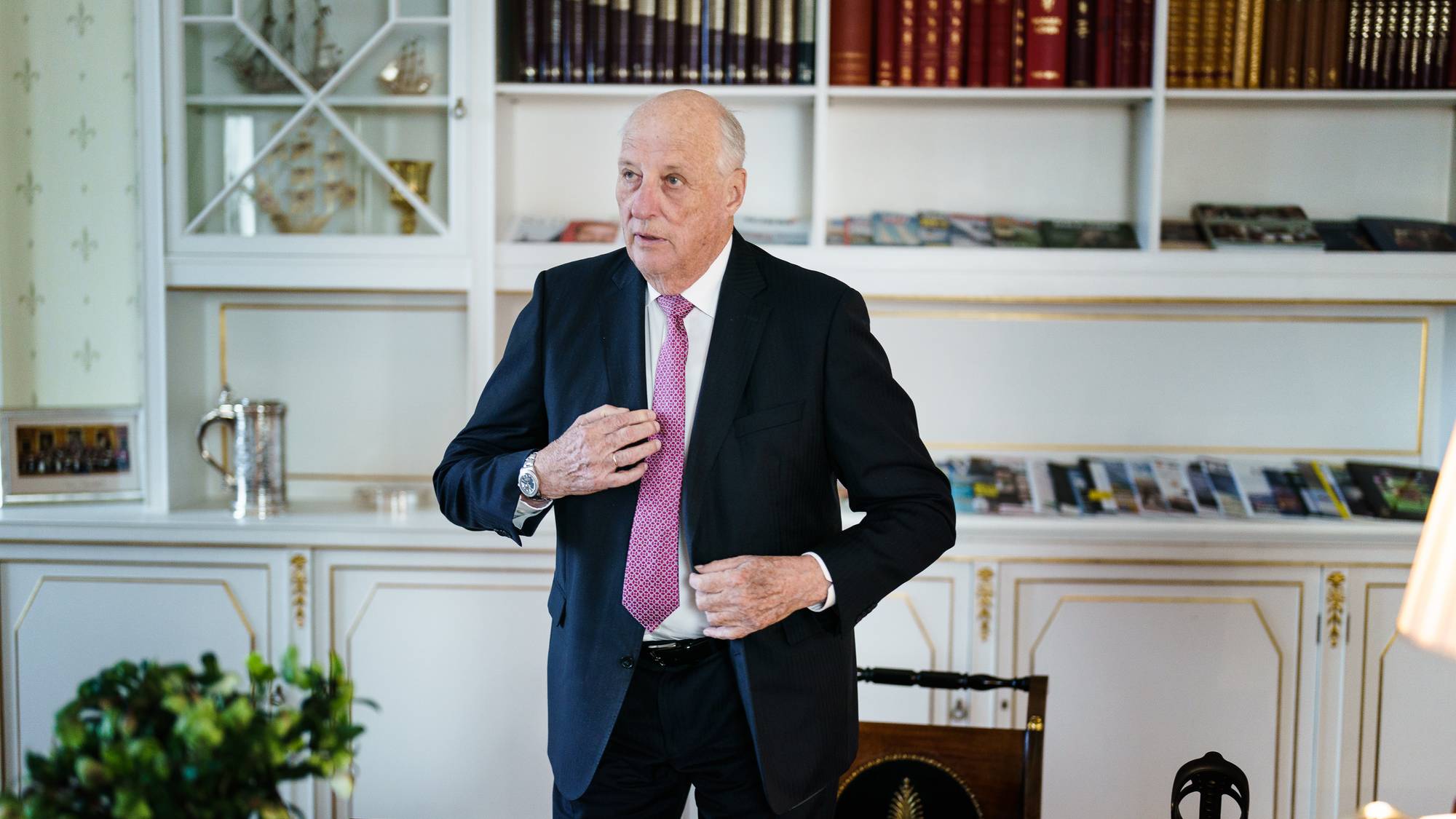 Kong Harald står bak skrivebordet på kontoret sitt på Slottet