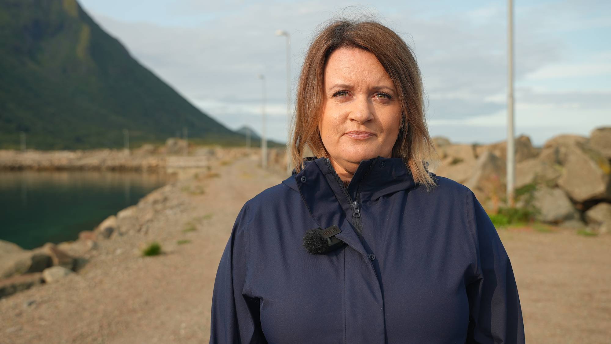 Lena Arntzen (H), ordfører i Hadsel står foran moloen til NorLens-anlegget i Fiskebøl utenfor Hadsel med blå jakke. Hun har lysebrunt hår og brune øyne.