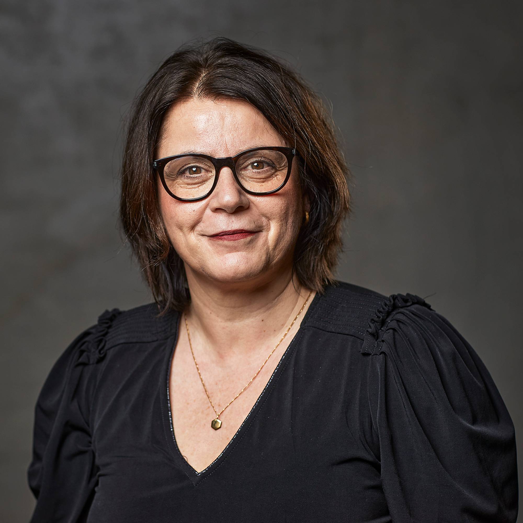 Ei kvinne med briller ser i kamera med et smil.