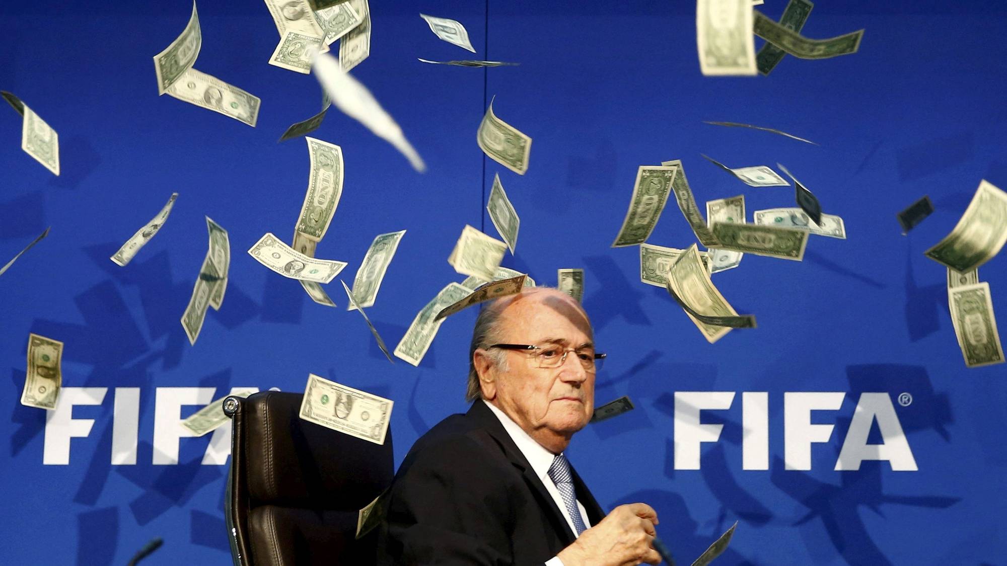 Sepp Blatter sitter foran en FIFA-bakgrunn mens amerikanske dollarsedler kastes over ham. (Bildebeskrivelsen er laget av en KI-tjeneste)