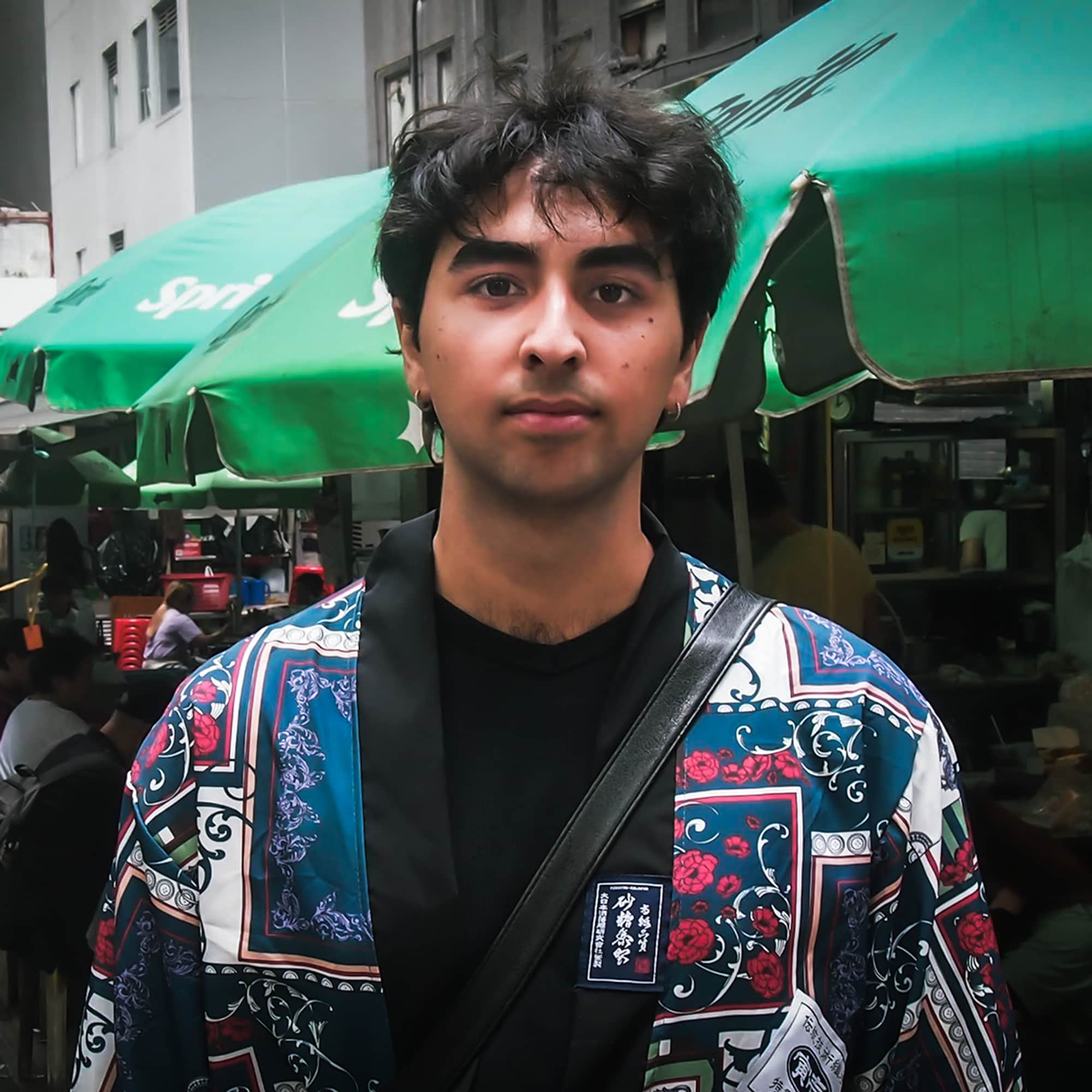 Fredrik (22) har mørkt hår og markerte øyebryn. Han står blant en folkemengde i Hong Kong. Han har et seriøst blikk.