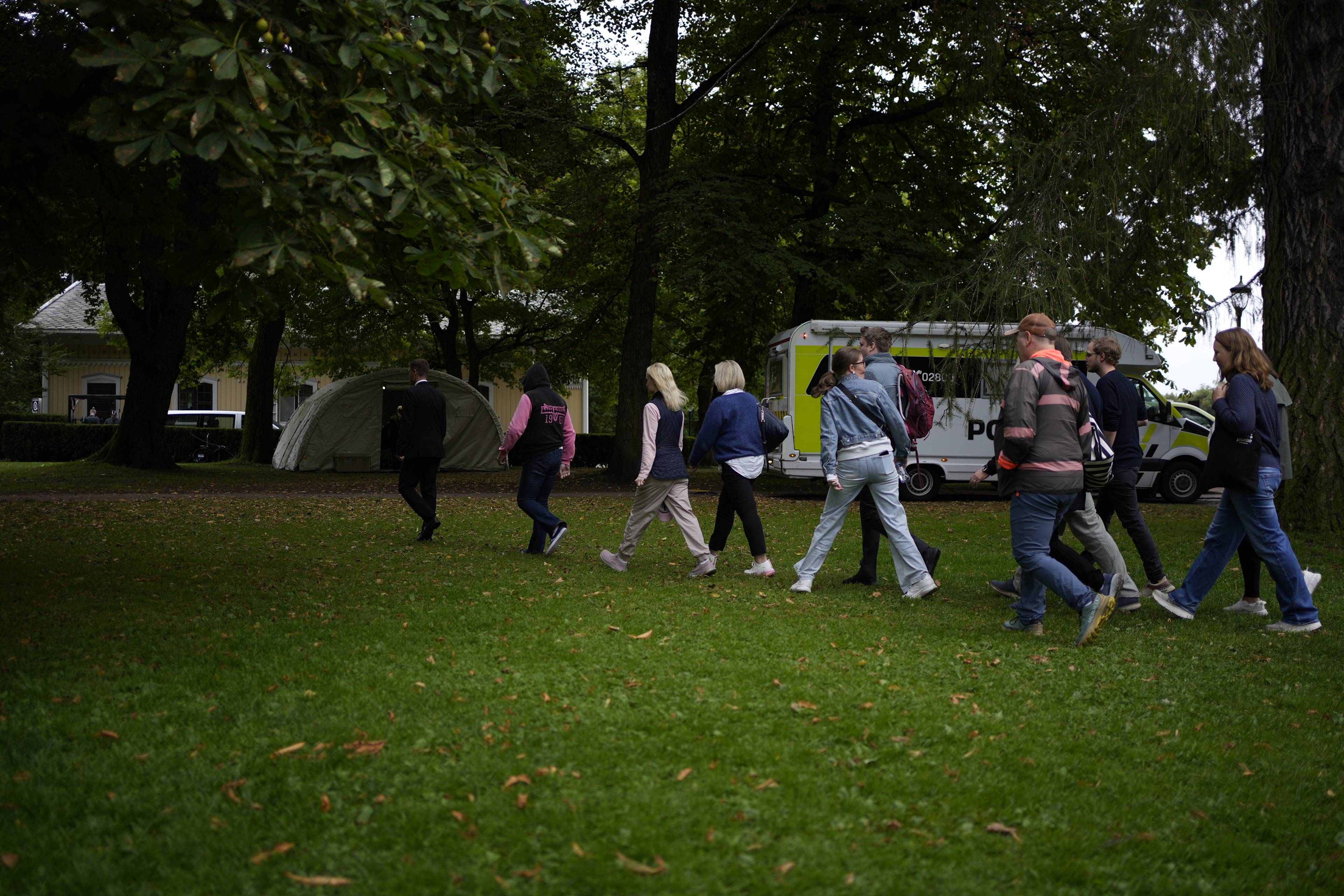 En gruppe personer går over en gressplen mot et telt i en park med en politibil i bakgrunnen. (Bildebeskrivelsen er laget av en KI-tjeneste)