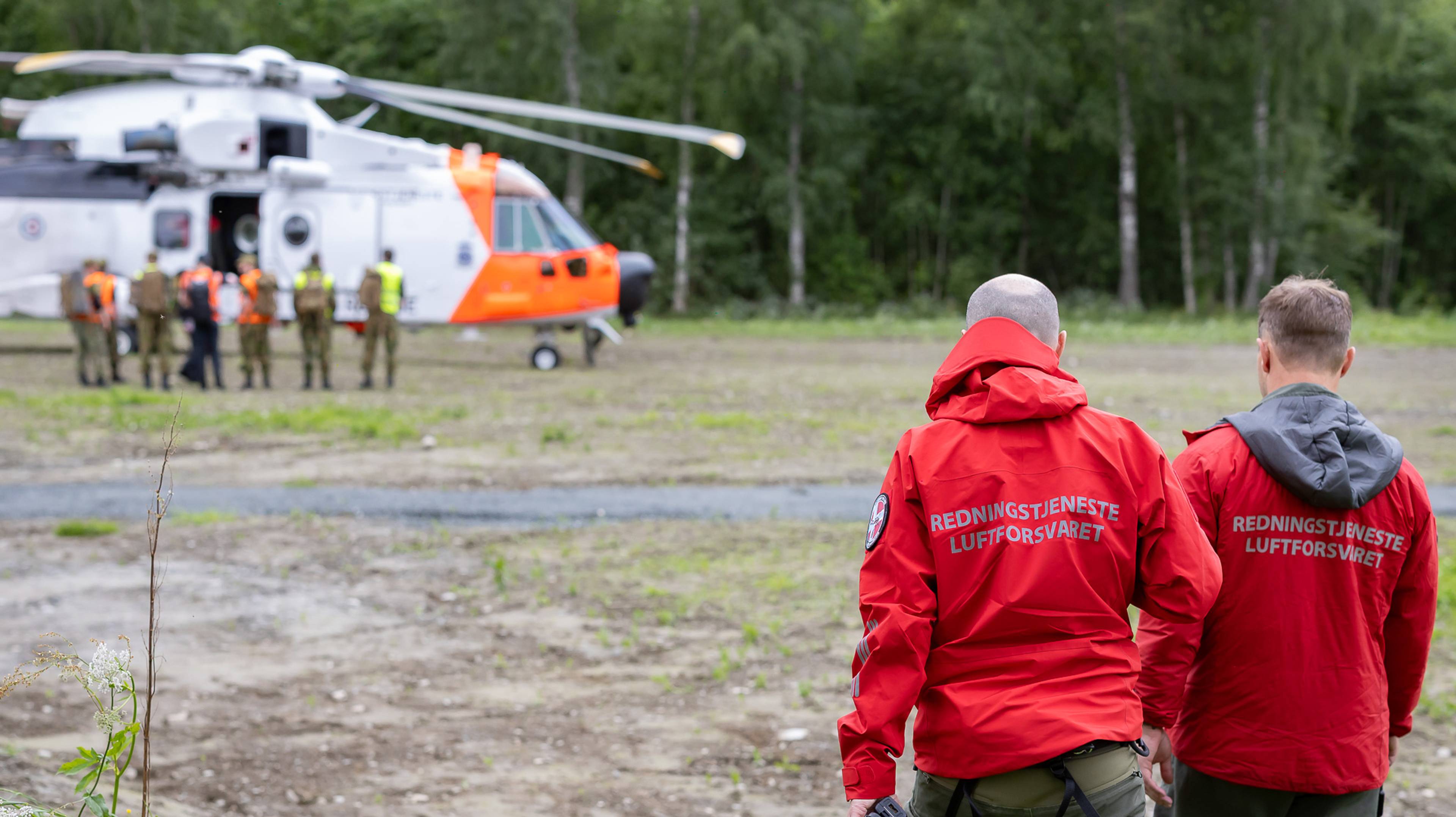 Letemannskap er i ferd med å gå om bord i et redningshelikopter. I forgrunnen av bildet ser vi to fra 330 skavdronen på Ørland. På ryggen står det "Redningstjeneste luftforsvaret"