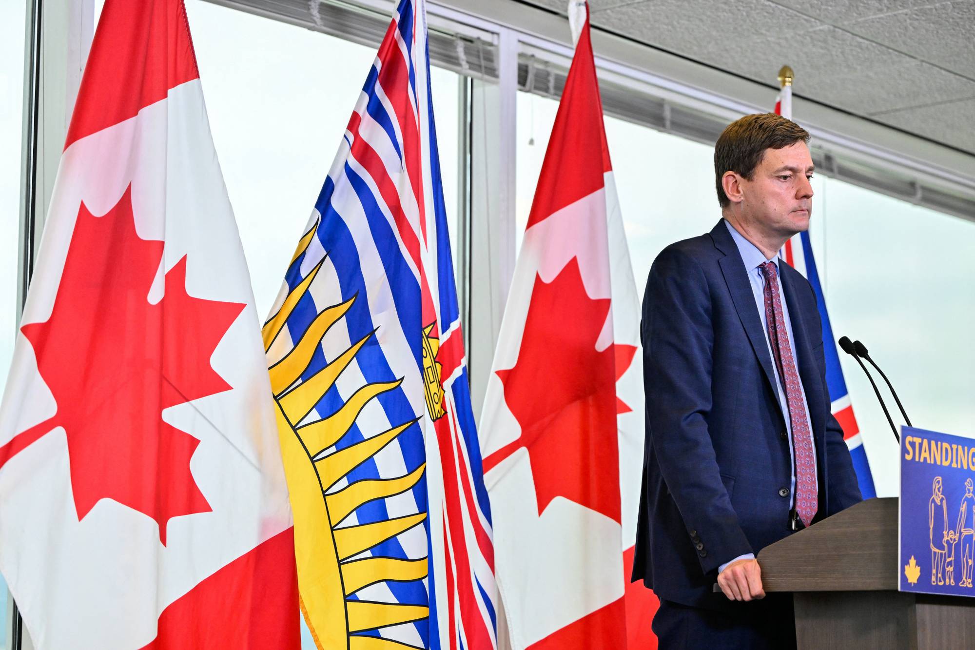 British Columbias delstatsminister David Eby står ved siden av kanadiske flagg. 