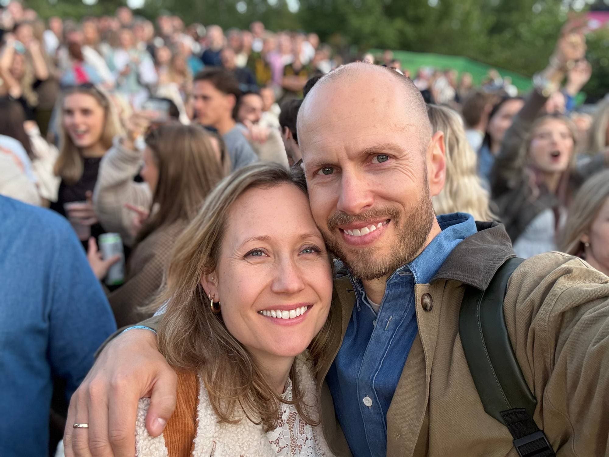 en mann og en kvinne poserer for et bilde med en folkemengde bak seg (Bildebeskrivelsen er laget av en KI-tjeneste)
