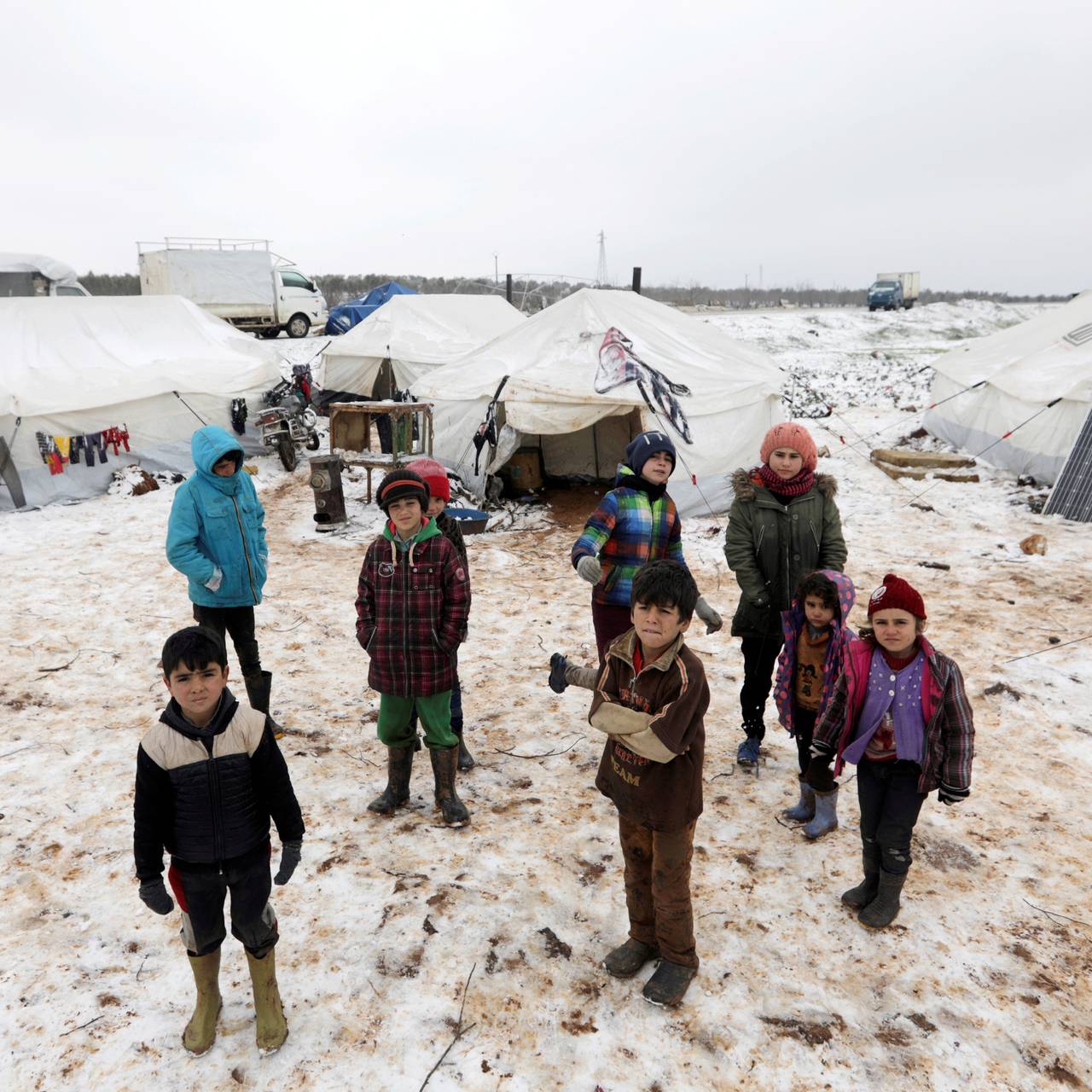 Syriske barn og voksne står i snøen ved telt i en flyktningleir i Azaz i Syria.
