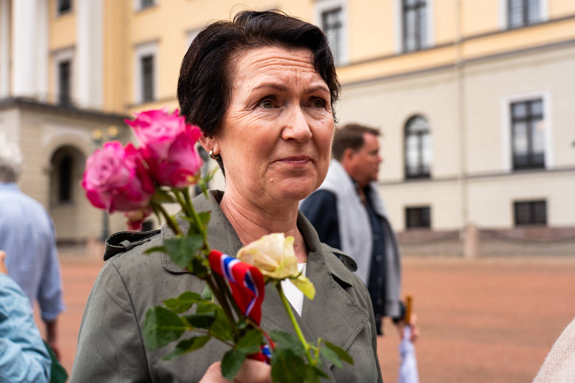 Kvinne holder roser med norsk sløyfe foran Slottet. (Bildebeskrivelsen er laget av en KI-tjeneste)