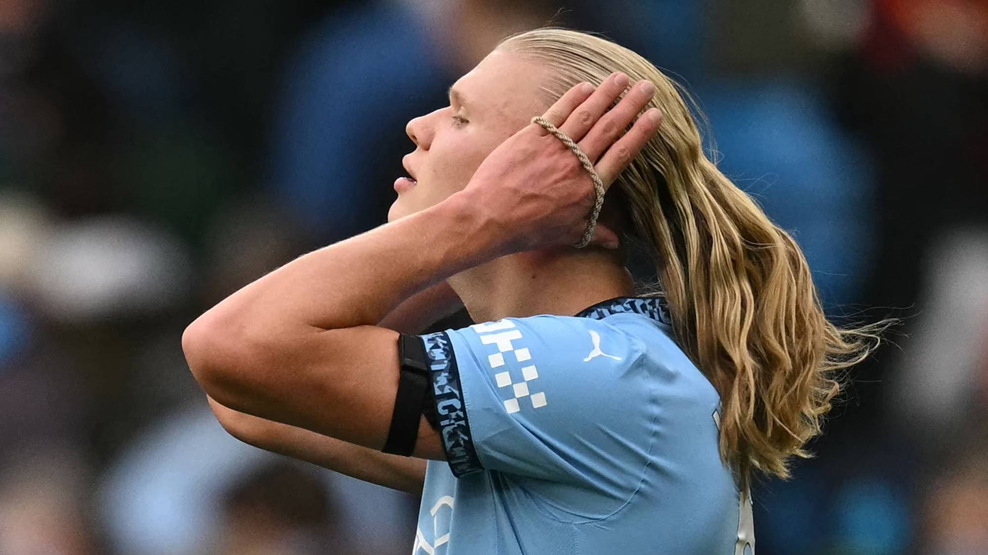 Erling Braut Haaland tar seg til håret iført lyseblå fotballdrakt. (Bildebeskrivelsen er laget av en KI-tjeneste)