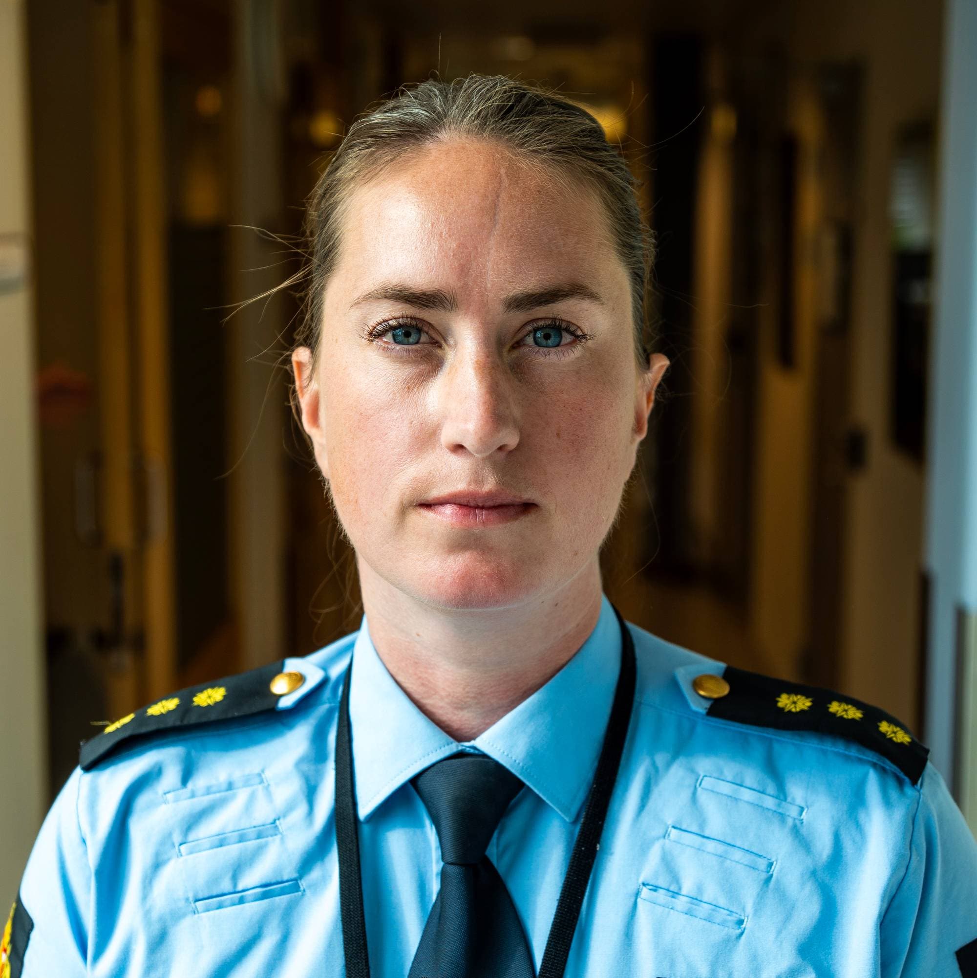 Portrett av en kvinnelig politibetjent i uniform stående i en korridor.