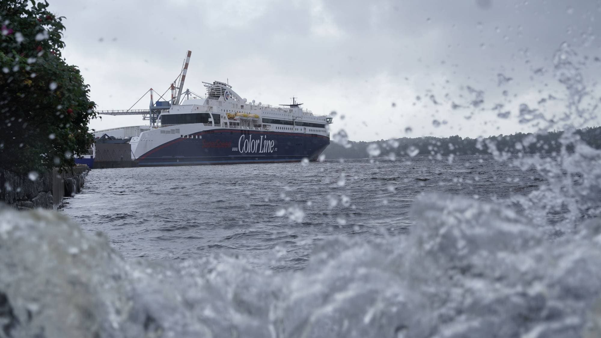 Color Line-ferge til kai ved en havn med vannsprut i forgrunnen. (Bildebeskrivelsen er laget av en KI-tjeneste)