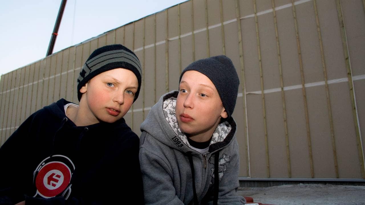 En ung Benjamin lener seg inn i bildet, mot en litt eldre gutt. Begge har luer og hettegensere på.