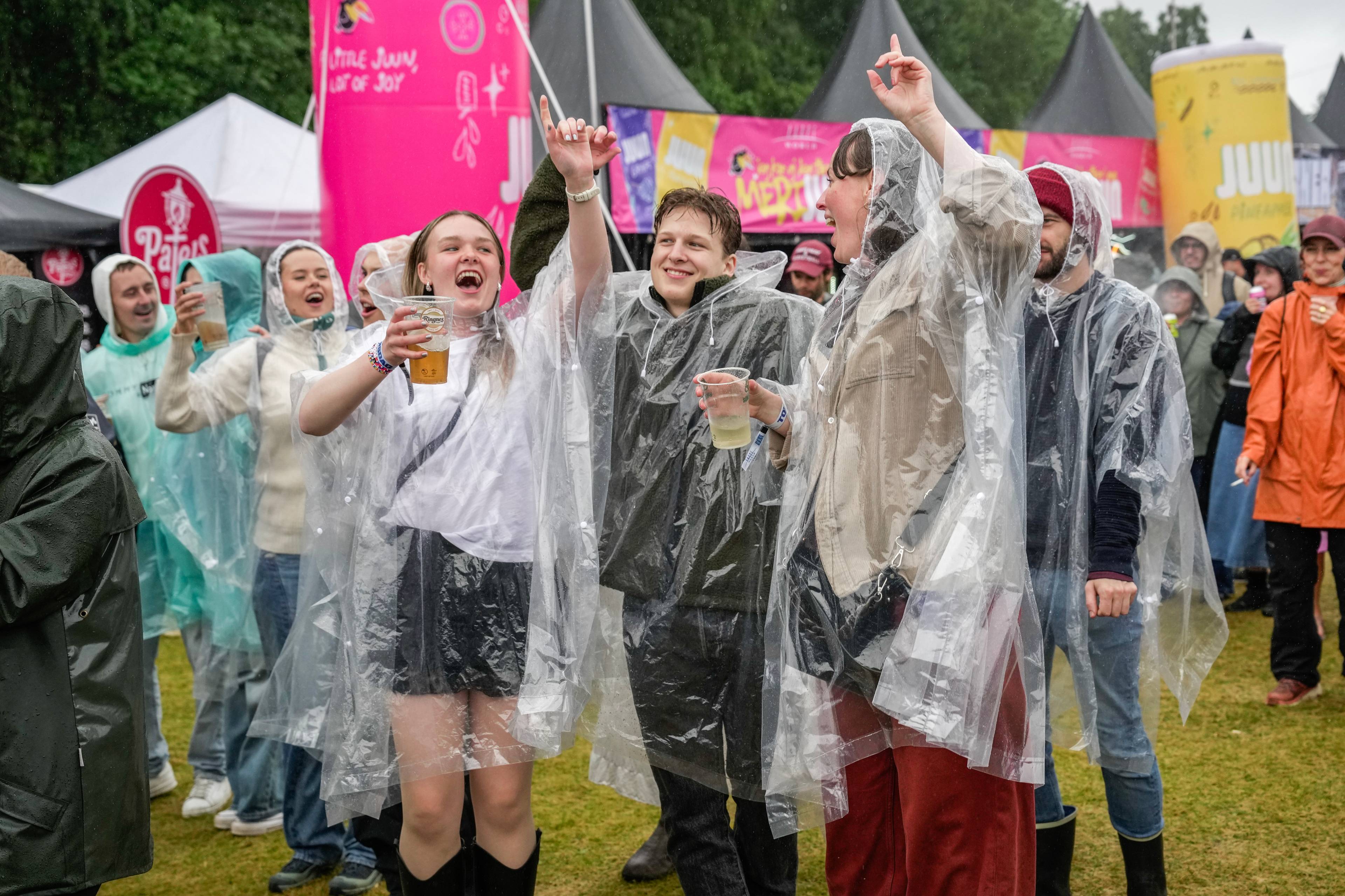 Publikum i regnponchoer feirer på musikkfestival med drikke i hendene. (Bildebeskrivelsen er laget av en KI-tjeneste)