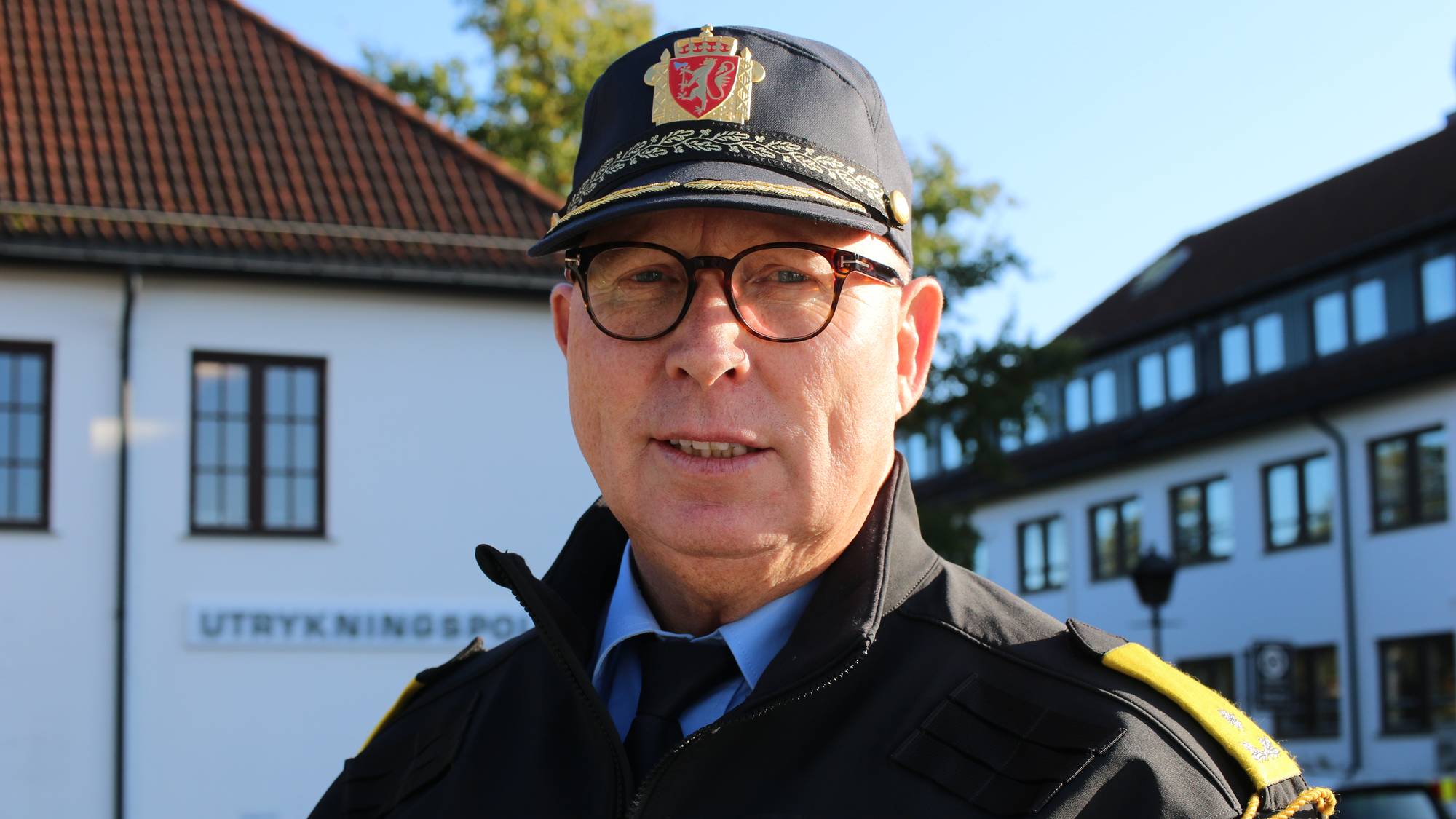 en mann i tolluniform står foran et hvitt bygg (Bildebeskrivelsen er laget av en KI-tjeneste)