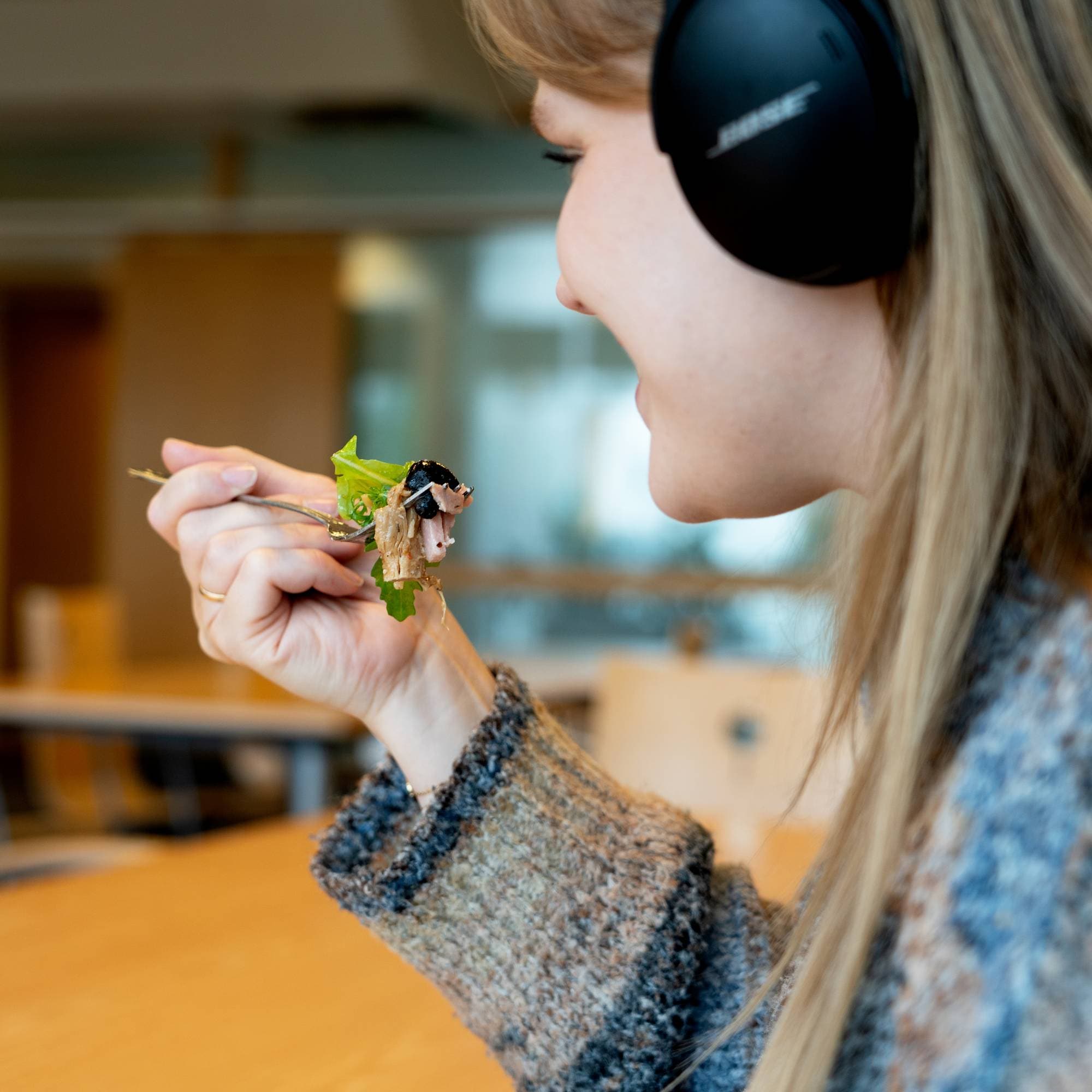 En kvinne med langt hår spiser mat mens hun hører på musikk i hodetelefoner.