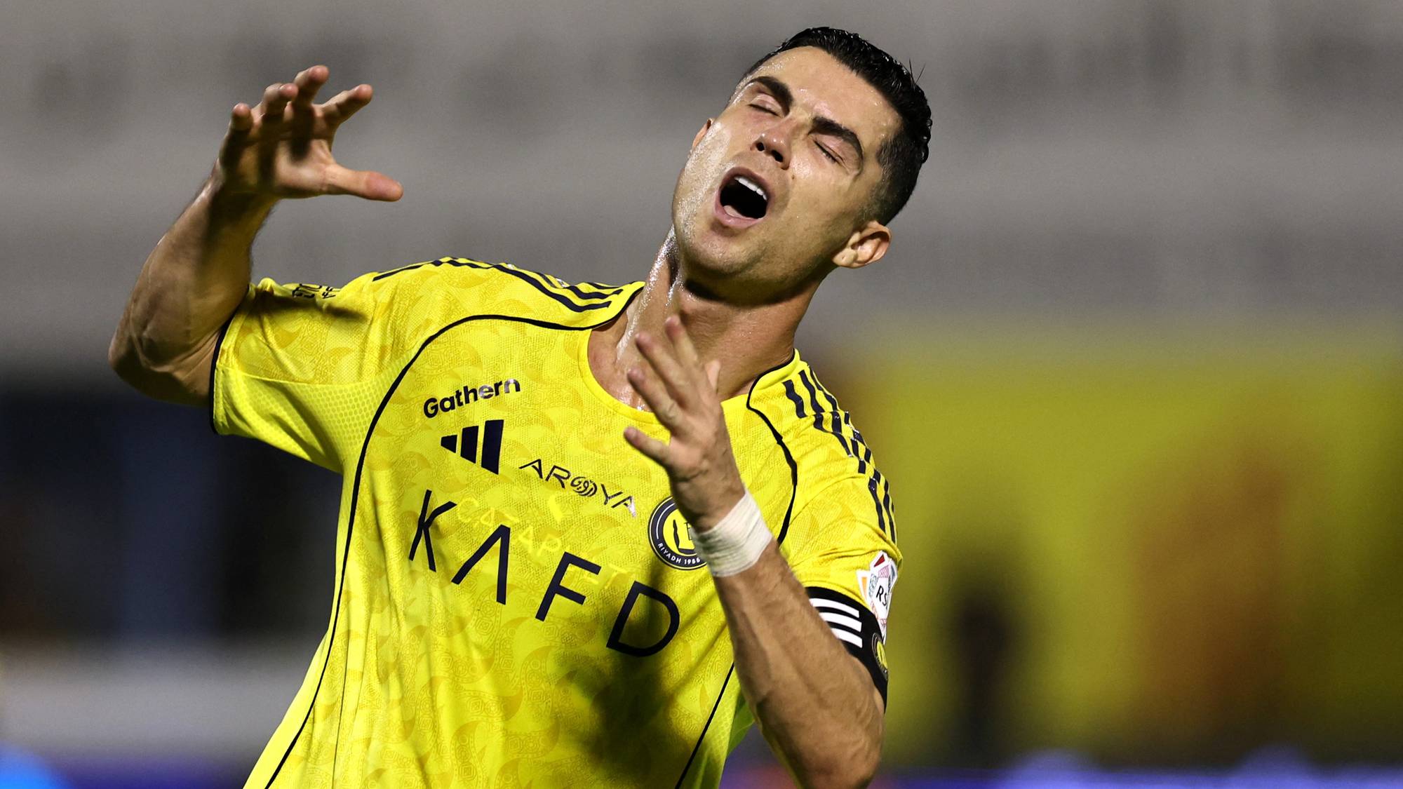 Fotballspilleren Cristiano Ronaldo med ansiktet mot himmelen og hendene løftet. Han bærer en gul trøye med sponsornavn. Bakgrunnen er uskarpt. (Bildebeskrivelsen er laget av en KI-tjeneste)