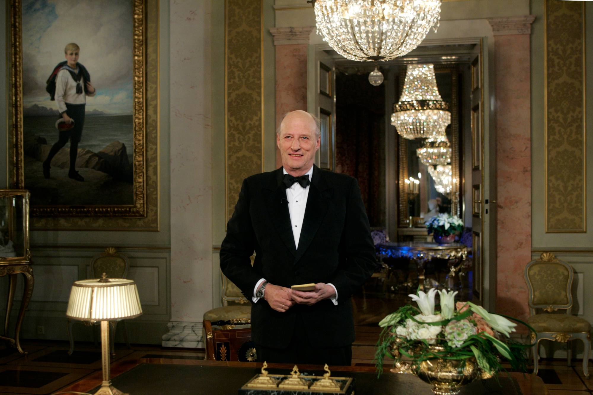 Kong Harald står i smoking i en stue på Det kongelige slott. Han holder et ark i hendene. (Bildebeskrivelsen er laget av en KI-tjeneste)