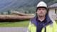 Arne Stubhaug / NRK Mann med vernehjelm foran store rør på et anleggsområde ved en fjord. (Bildebeskrivelsen er laget av en KI-tjeneste)