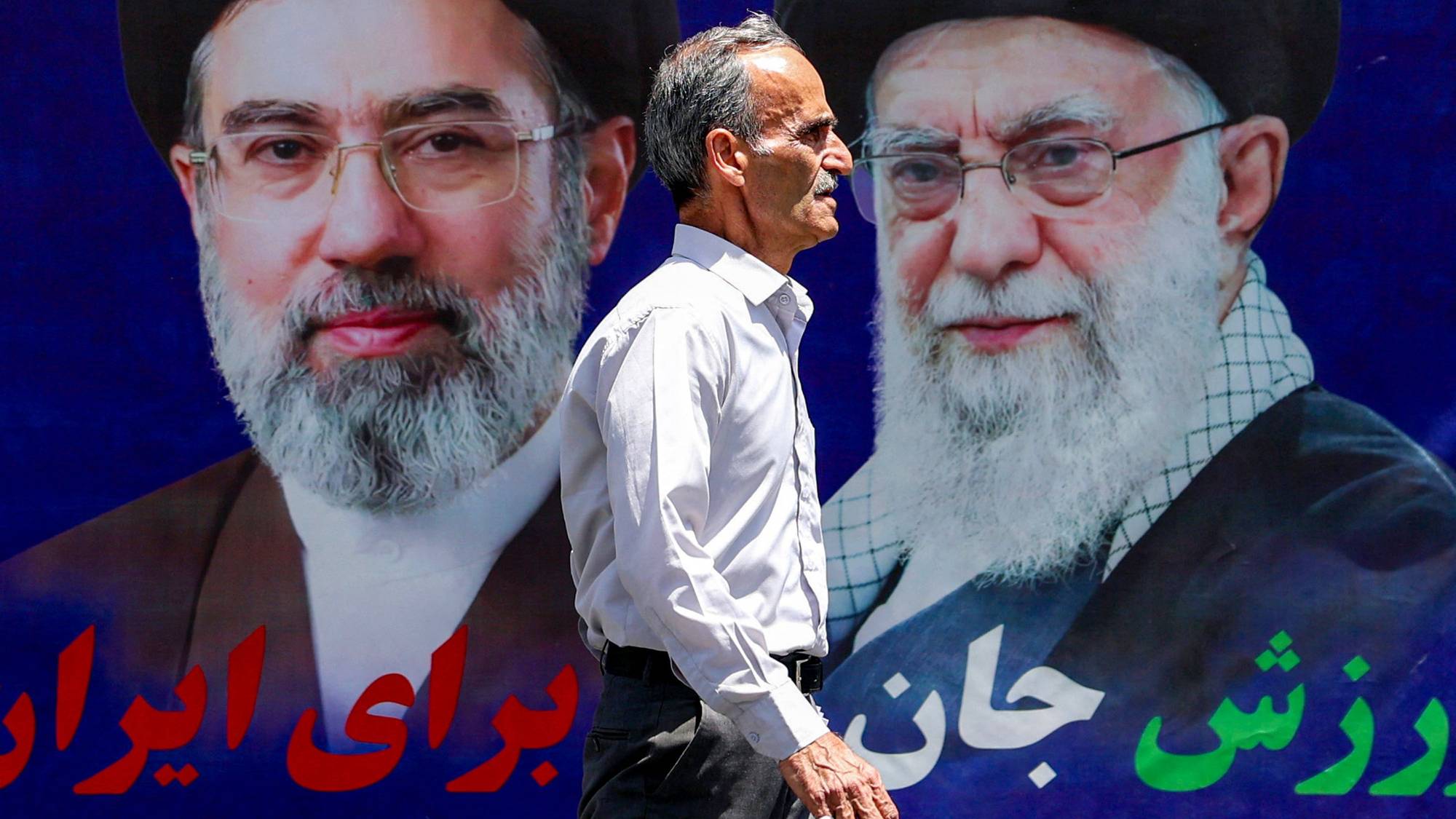 En mann går forbi en stor plakat av Irans leder Mojtaba Khamenei og hans far, tidligere leder Ali Khamenei.