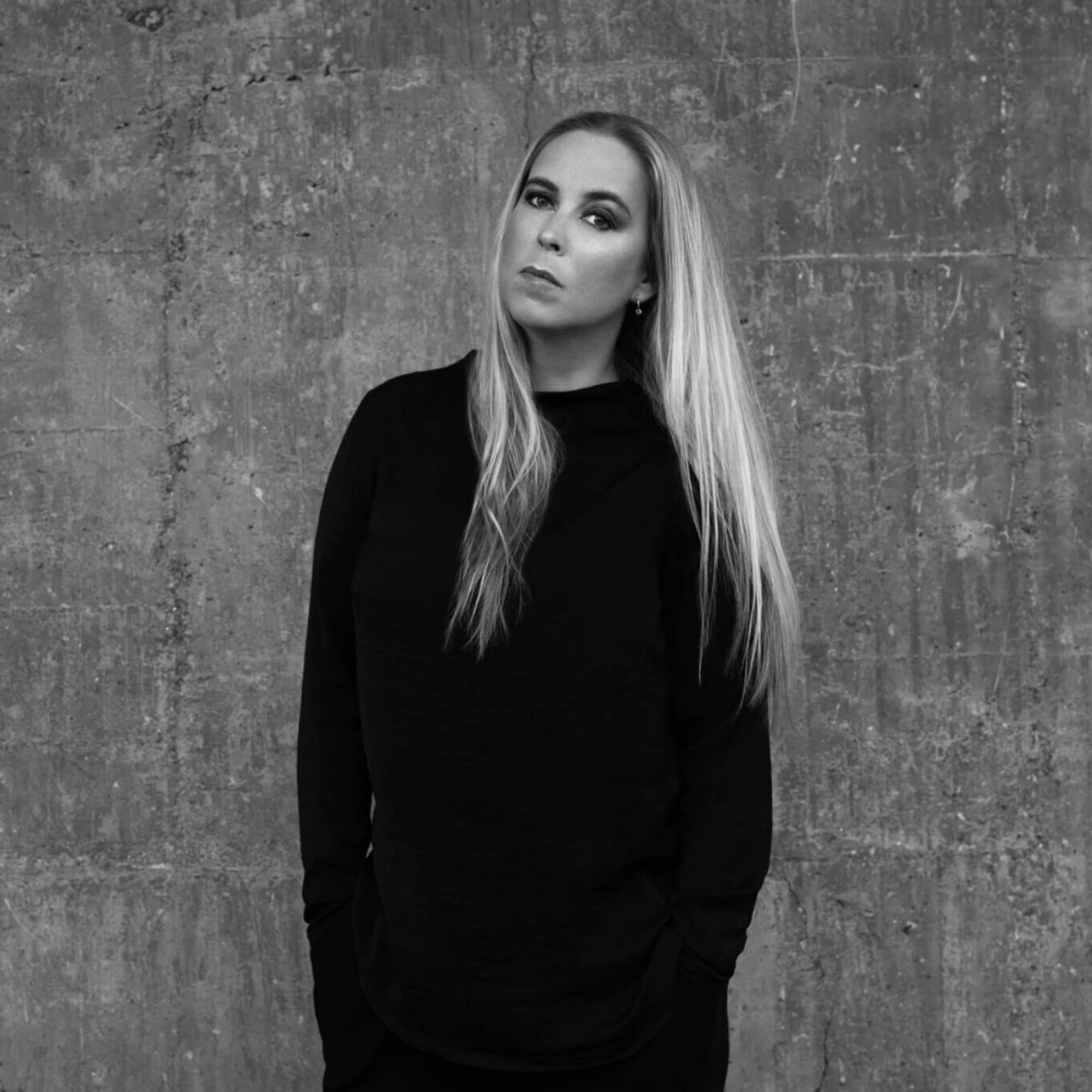 Vi ser en kvinne foran en vegg. Det er låtskriveren Anne Judith Wik som ser mot fotografen.