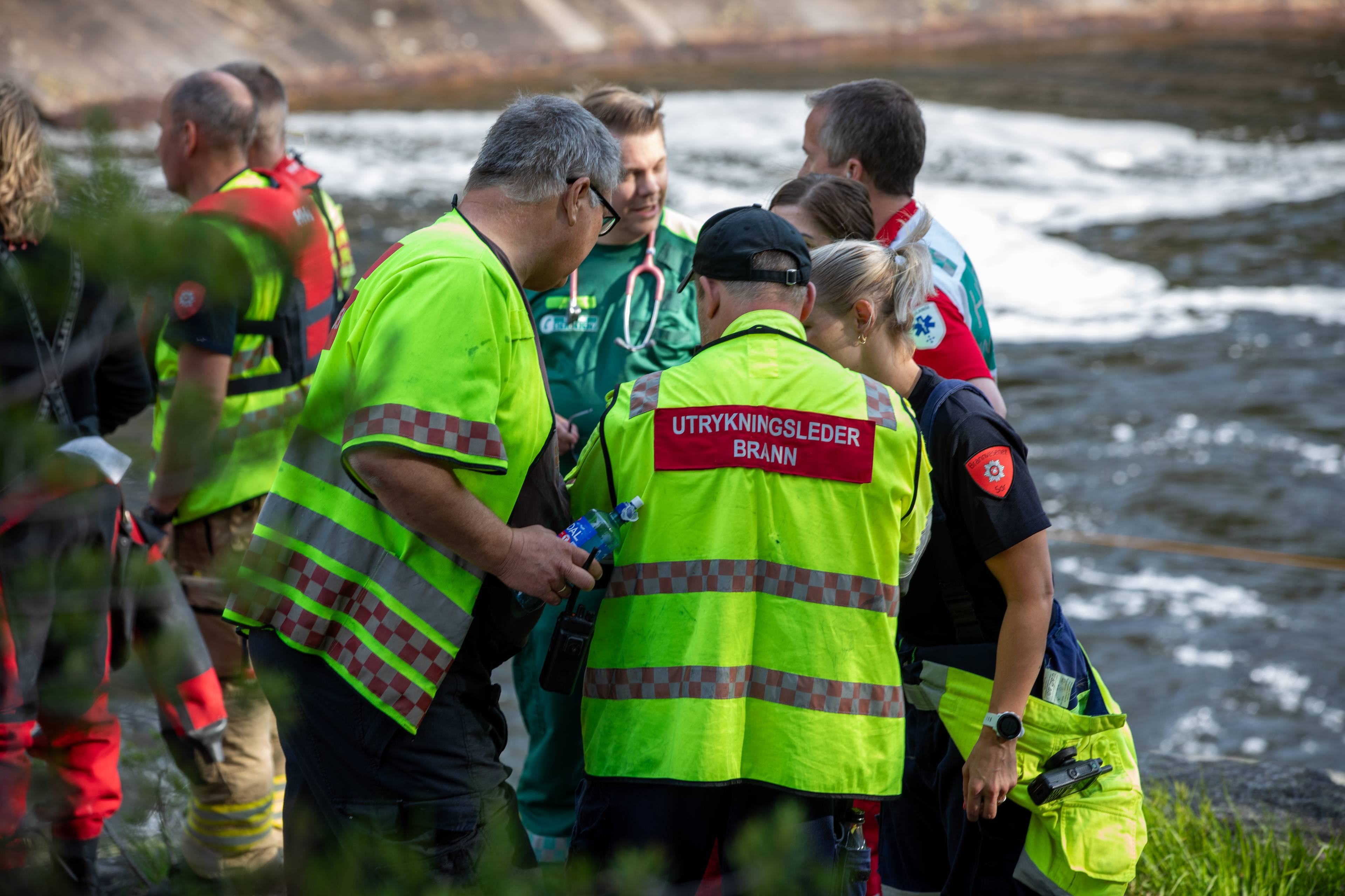 Redningsmannskaper i uniform samlet ved en elv under en operasjon. (Bildebeskrivelsen er laget av en KI-tjeneste)