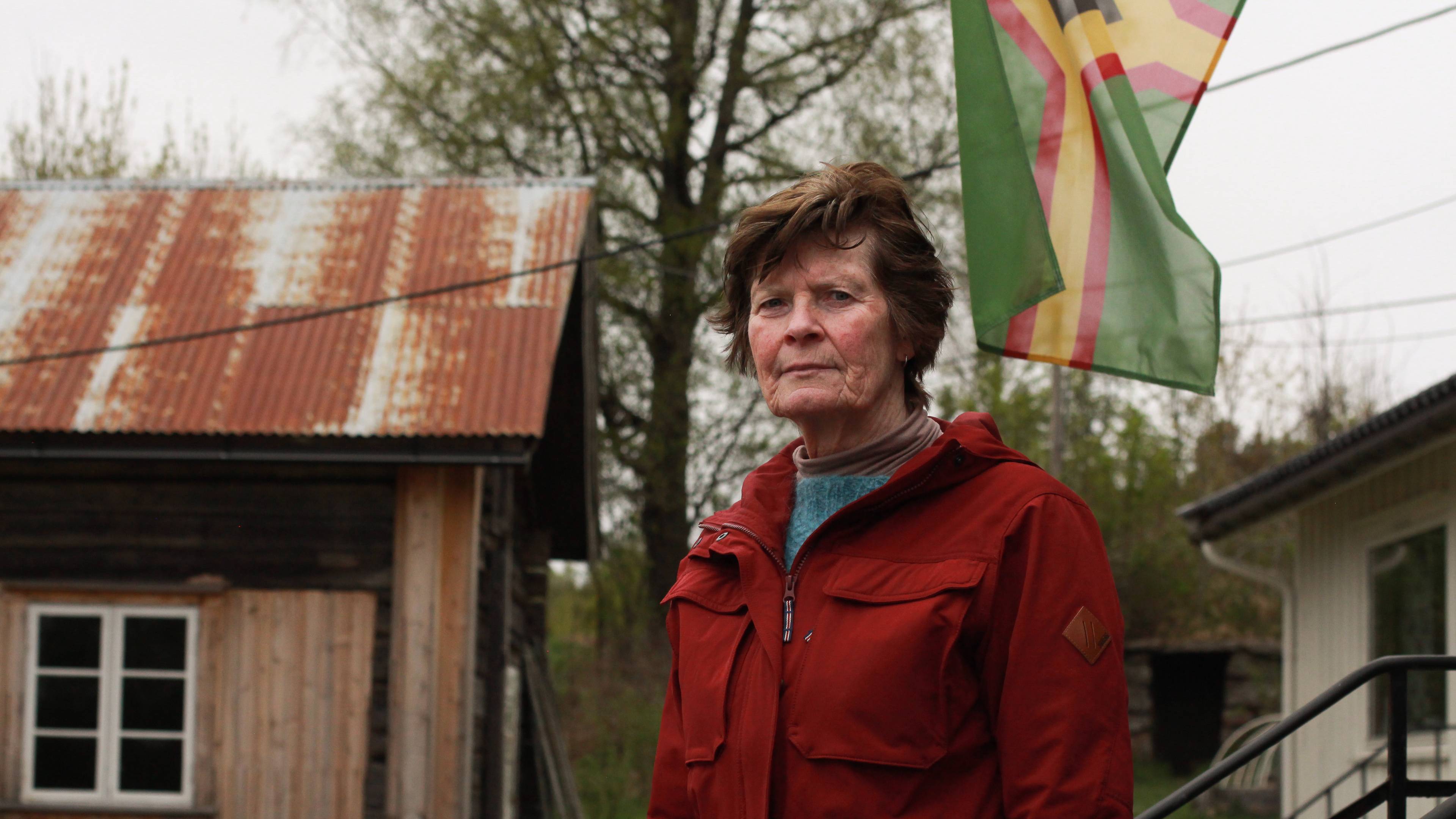 en eldre kvinne med kort brunt hår og rød jakke går rundt på et småbruk