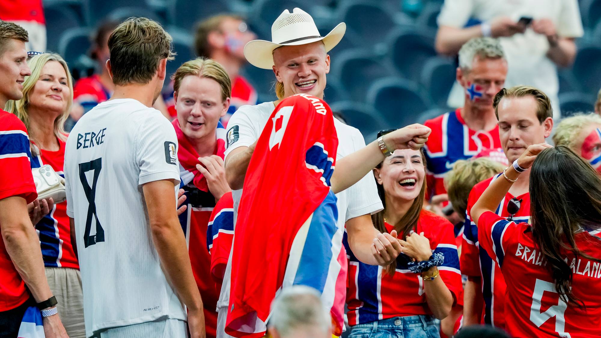 Erling Braut Haaland med cowboyhatt møter supportere på tribunen under en fotballkamp. (Bildebeskrivelsen er laget av en KI-tjeneste)